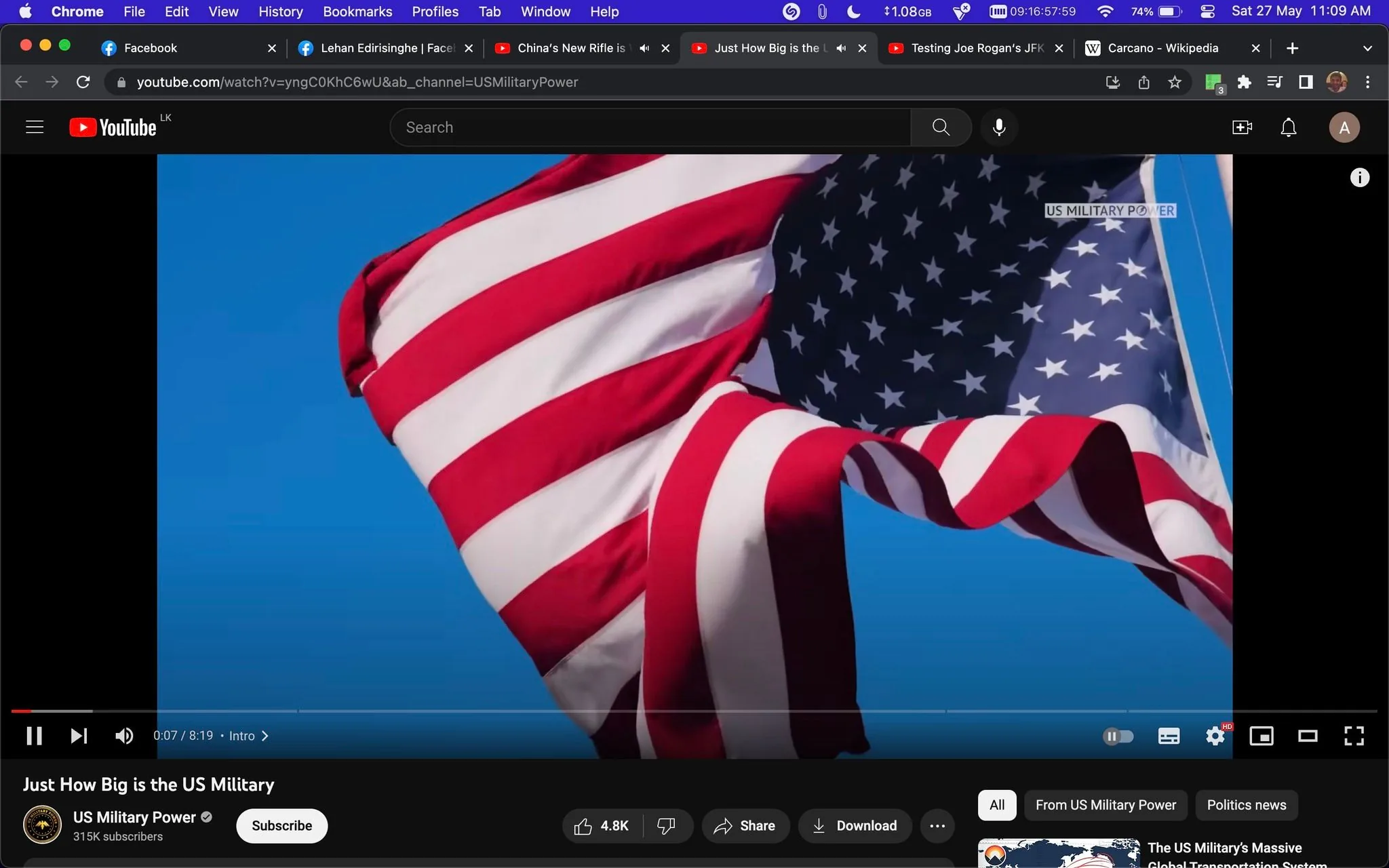 The screenshot shows a YouTube video titled "Just How Big is the US Military" uploaded by the channel "US Military Power." The video is currently paused at 0:07 of its total 8:19 runtime. The main image features a close-up of the American flag waving against a clear blue sky, symbolizing patriotism and national pride. The flag's red, white, and blue colors are vividly displayed, with the stars and stripes prominently visible. The video is likely exploring the scale and capabilities of the United States military. Text overlay on the image reads "US MILITARY POWER," emphasizing the video's focus on military strength. The user interface shows options to like, share, download, and subscribe to the channel, which has 315K subscribers. The top of the screen is filled with various browser tabs, indicating a desktop viewing experience.