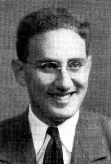 The image is a black and white portrait of a young Henry Kissinger. He is wearing a formal suit and tie, which is typical of mid-20th-century attire. His hair is neatly combed, and he is wearing glasses with a slight smile on his face, suggesting a pleasant or approachable demeanor. The photograph has a classic studio portrait quality, with soft lighting that highlights his facial features without any harsh shadows. The background is plain, keeping the focus on Henry Kissinger himself. The image captures a moment in time likely from his early years before he became widely recognized on the international stage. The overall mood is composed and professional, characteristic of formal portrait photography of that era.