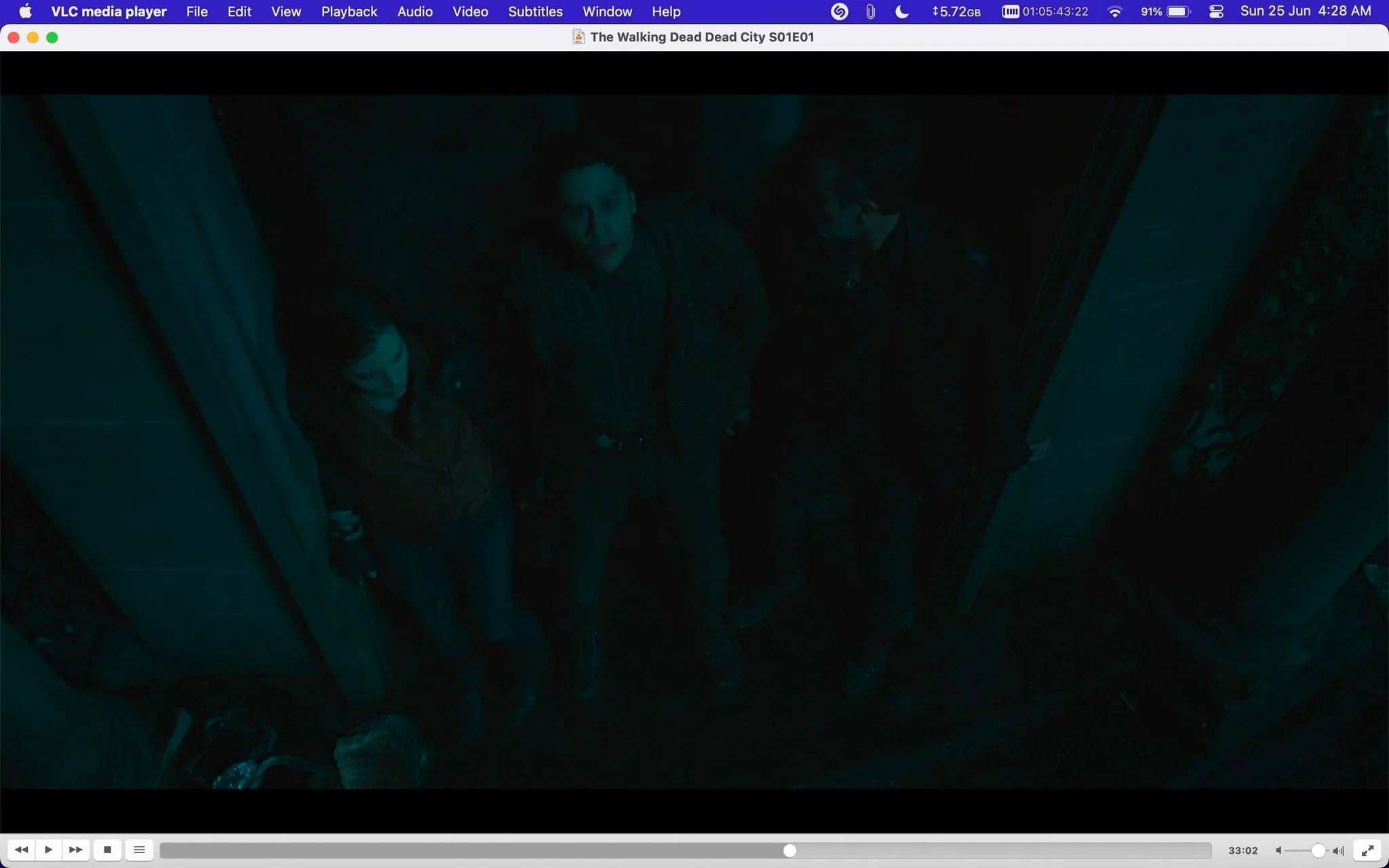 ```
1) The screenshot shows a scene from "The Walking Dead Dead City S01E01" being played on VLC media player. The image captures three individuals standing closely in a dimly lit indoor setting. The lighting is dark and has a bluish tint, creating a tense and mysterious atmosphere typical of the "The Walking Dead" series. The person in the middle seems to be looking upwards with a concerned expression, while the two others are standing to the side. One of them leans against a wall, and the other is partially in shadow. They are dressed in rugged, practical clothing suitable for survival scenarios, suggesting a post-apocalyptic environment. The scene is framed from above, looking down on the characters, which adds to the feeling of being watched or threatened. The media player’s interface is visible, showing controls and playback details, including a time stamp and file size.
2) On-screen text block:
- Title: "The Walking Dead Dead City S01E01"
- Site / app: "VLC media player"