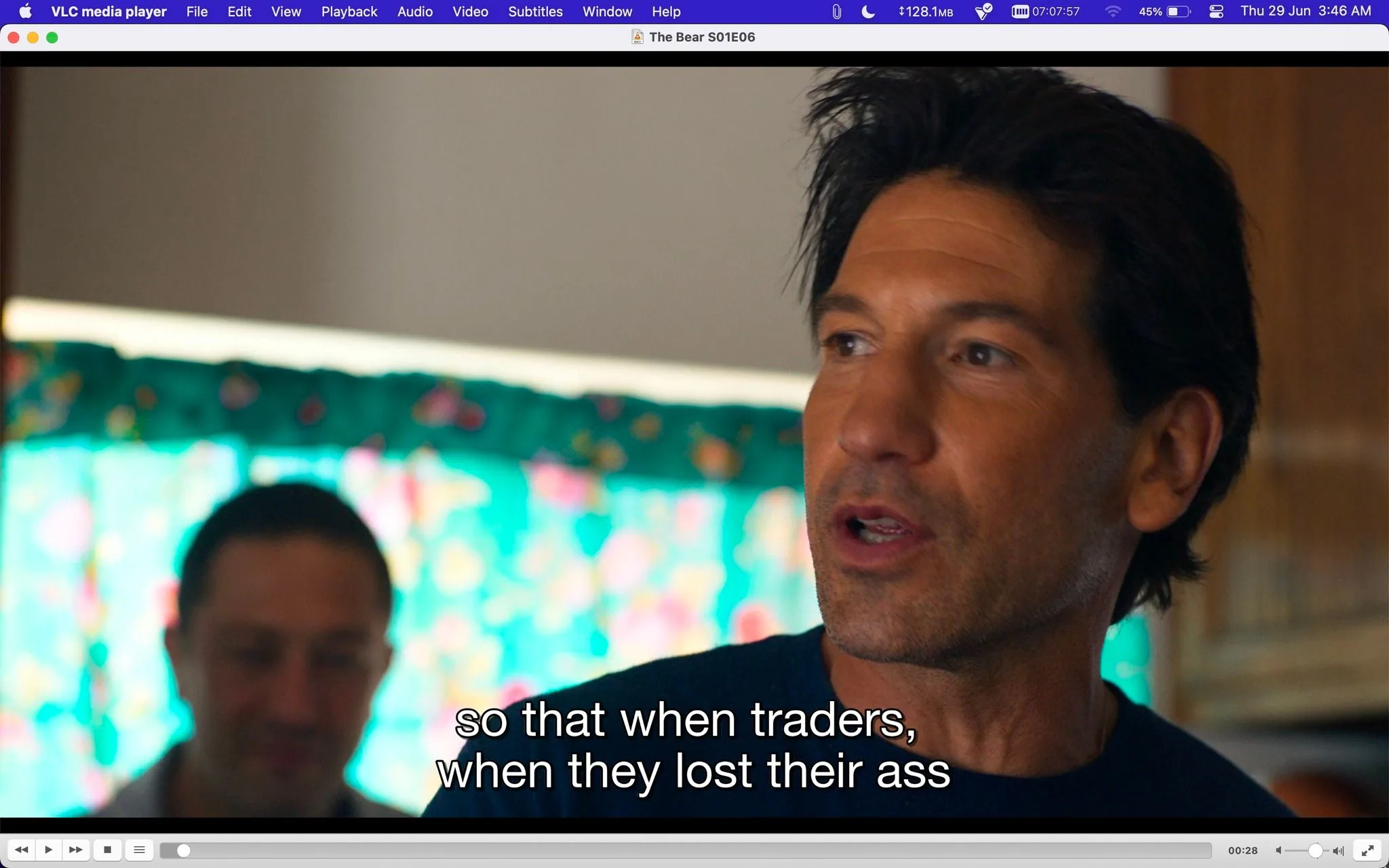 In this image, a scene from the show "The Bear" is displayed, specifically from episode 6 of season 1. The image is a screenshot taken from VLC media player, as indicated by the app's interface visible at the top. The title of the episode is shown on the player interface, confirming the source and context.
In the foreground, Jon Bernthall is prominently featured, speaking with a serious expression. The focus on his face suggests an intense or meaningful moment in conversation. Behind him, a blurred figure can be seen, and a colorful curtain provides a vibrant background. The lighting is warm, suggesting an indoor environment that feels intimate and personal. The subtitles read, "so that when traders, when they lost their ass," hinting at a financial or business-related discussion.
The entire scene is framed closely, highlighting the character's emotions and expressions. The colors in the background contrast with the natural skin tones, adding visual interest to the composition. This close-up style enhances the drama and intensity of the conversation depicted.