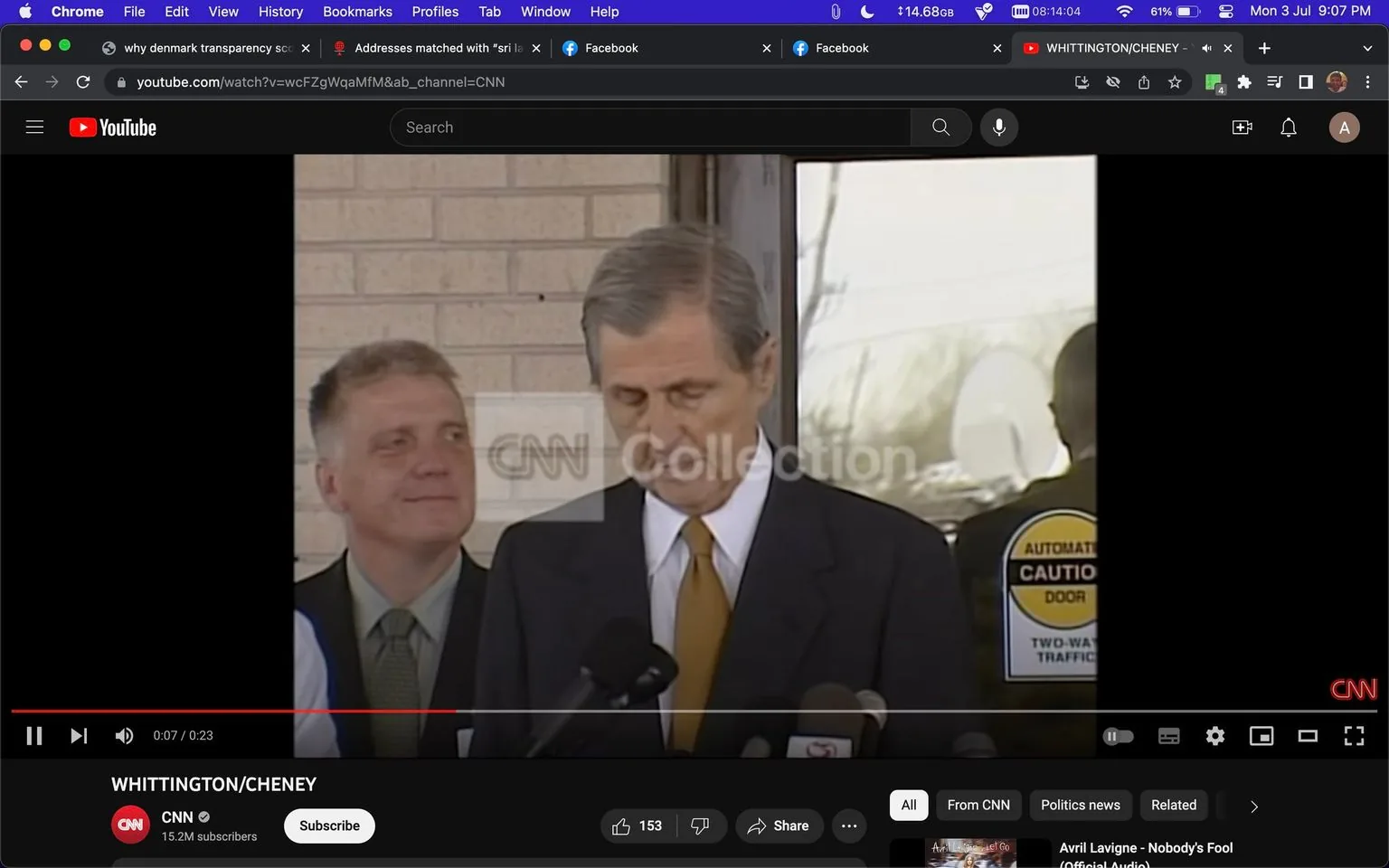 ```
The image is a screenshot from a YouTube video titled "WHITTINGTON/CHENEY" on the CNN channel, which has 15.2 million subscribers. It shows a press conference setting with two men standing in the foreground. The man on the left is slightly smiling, wearing a suit with a green tie. The man on the right, who appears to be speaking at the microphones, has a serious expression and is wearing a dark suit with a white shirt and a yellow tie. Behind them is a door with a sign that reads "AUTOMATIC CAUTION DOOR" and "TWO-WAY TRAFFIC". The background is a neutral brick wall. The CNN logo is visible in the bottom right corner, and there's a watermark that reads "CNN Collection" near the center. The overall mood is formal and serious, typical of a news briefing.