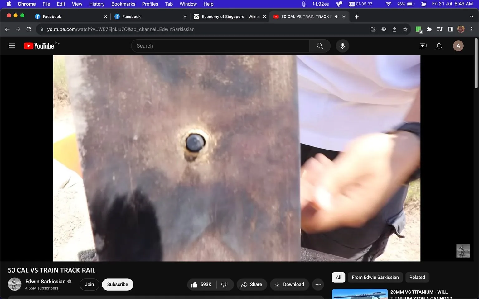 The image is a screenshot of a YouTube video titled "50 CAL VS TRAIN TRACK RAIL" from the channel Edwin Sarkissian. The scene captures a close-up view of what appears to be a bullet hole in a piece of metal, likely a train track rail. The metal surface is slightly discolored around the impact point, suggesting the force of the impact. To the right, a person's hand is visible, possibly gesturing or pointing at the hole, wearing a watch and white shirt. The lighting is bright, indicating it is taken outdoors, possibly in a sunny environment. The video seems to be an experimental demonstration involving firearms and metal durability. The YouTube interface shows engagement metrics like likes and subscription options, with a visible tab bar at the top indicating multiple open browser tabs, suggesting active multitasking or research.
- Title: "50 CAL VS TRAIN TRACK RAIL"
- Channel / profile: "Edwin Sarkissian"
- Site / app: "YouTube"
