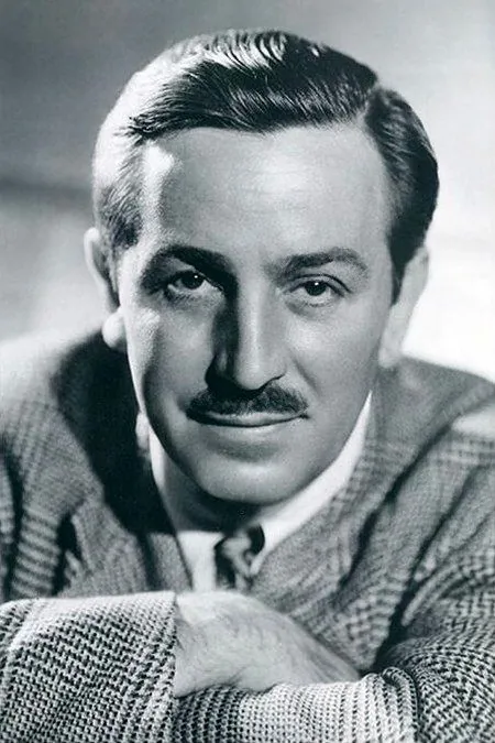 Walt Disney is depicted in this classic black and white portrait. The image captures him in a formal setting, likely a studio, given the controlled lighting and posed composition. Walt Disney is portrayed with a slight, confident smile, looking directly at the camera. His hair is neatly combed back, and he sports a well-groomed mustache. He is dressed in a checkered jacket, a white shirt, and a tie, exuding a professional demeanor. The lighting highlights his facial features, creating a sharp contrast with the background, which is softly out of focus. His posture suggests ease and authority, reflective of his status as a prominent figure in the entertainment industry. The photograph is a testament to his enduring legacy, capturing not just his likeness but the charisma that defined his persona.