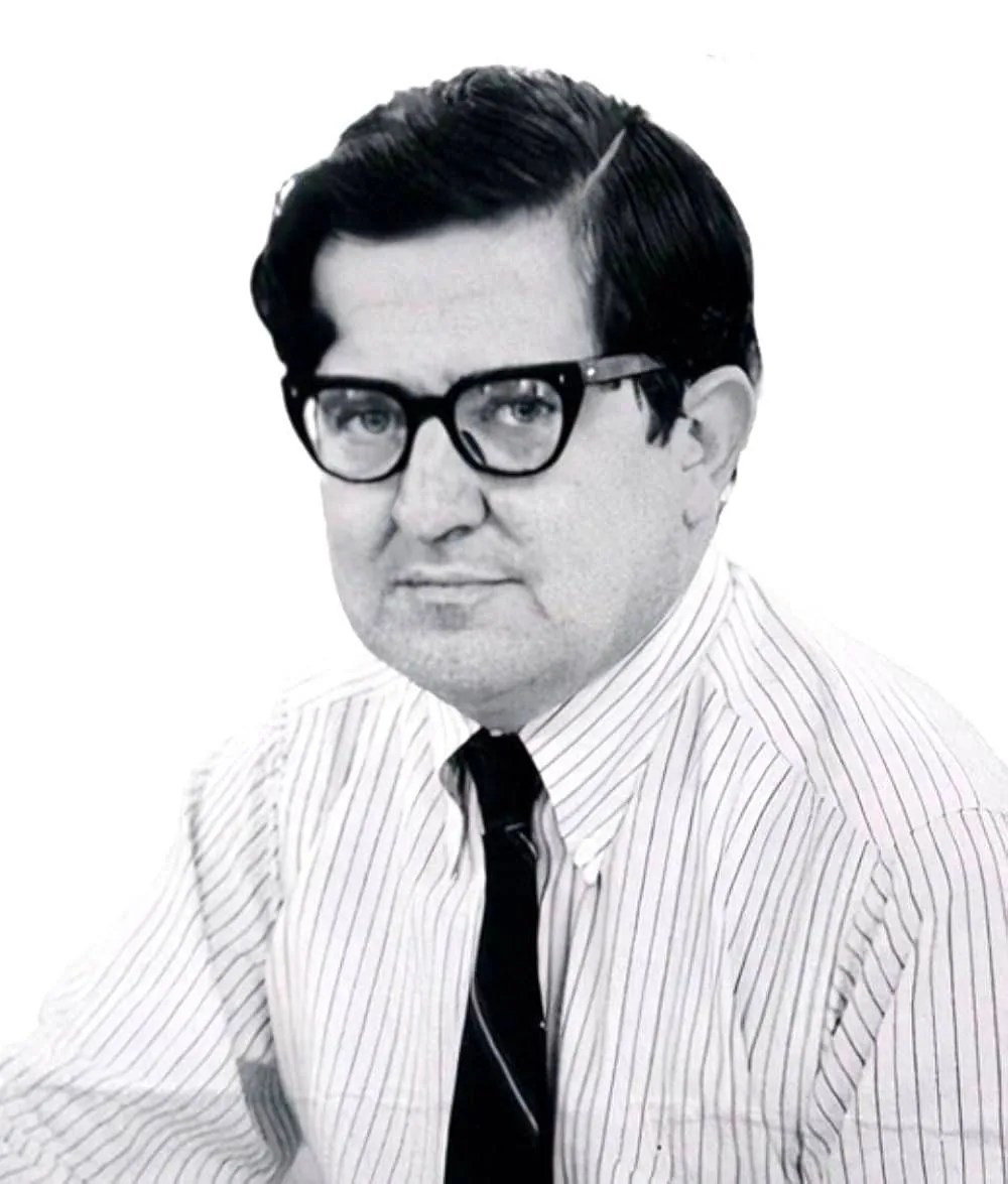 This black and white portrait features AM Rosenthal, displaying a formal and professional demeanor. He is seated, facing slightly to the side, with a neutral expression. Rosenthal is wearing a striped dress shirt paired with a dark tie, indicative of a formal or business setting. His dark, neatly combed hair and thick-rimmed glasses contribute to a scholarly or authoritative appearance. The background is plain, which focuses attention on Rosenthal himself, suggesting this could be a professional portrait used for official purposes, such as a publication or a corporate biography. The lighting is soft and even, adding to the clarity and focus on his facial features. There are no visible objects or text in the image, maintaining the emphasis on his persona.