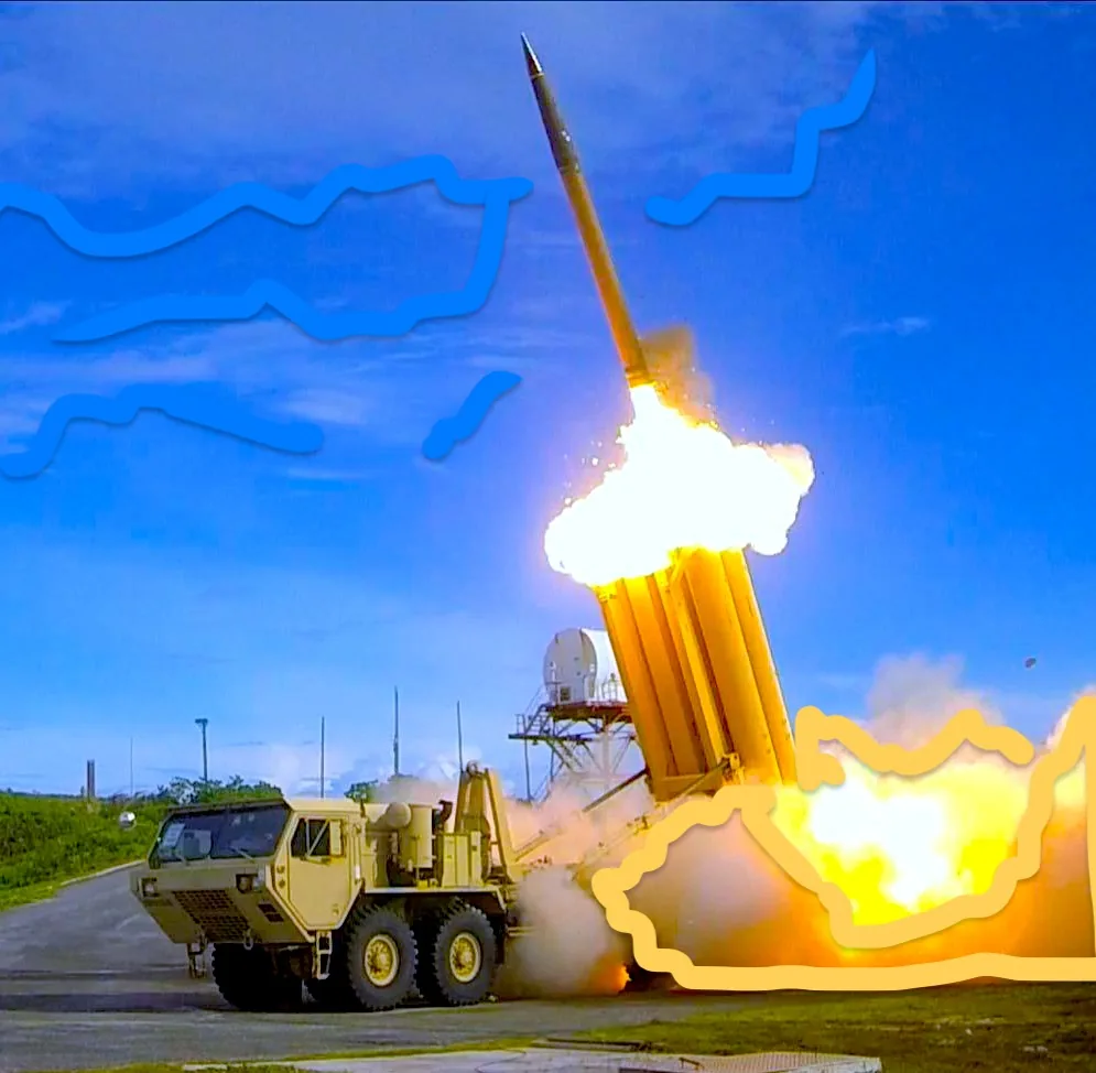 The image depicts a missile launch from a military vehicle. The scene is set outdoors under a clear blue sky with wispy clouds above. The missile is captured mid-launch, with bright flames and smoke erupting from its base. A tan military vehicle with six wheels is stationed beside the launching system, which appears to be part of a missile defense system. The background reveals a radar installation, indicating a testing or military base environment. The bright colors from the launch contrast with the serene blue of the sky, creating a dramatic visual effect. The energy of the launch is palpable, with the missile angled upward, suggesting rapid movement. No text or branding is visible in the image.