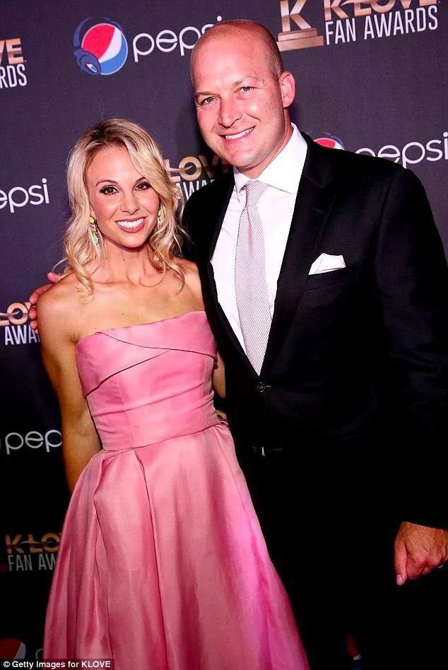 The image features Tim and Elisabeth Hasselbeck attending an event, specifically the KLOVE Fan Awards. They are posing together on the red carpet, showcasing a formal and celebratory atmosphere. Elisabeth is wearing an elegant pink strapless gown, accessorized with statement earrings, and her blonde hair is styled in loose waves, giving her a glamorous appearance. Tim is dressed in a classic black suit paired with a white shirt and a light pink tie, complementing Elisabeth's dress. Both are smiling warmly at the camera, suggesting a joyful and pleasant mood.
The backdrop prominently displays logos for "pepsi" and "KLOVE FAN AWARDS," indicating the event's sponsors or organizers. The lighting is bright and even, highlighting their attire and expressions. The overall composition captures a moment of celebration and recognition, typical of such award ceremonies.