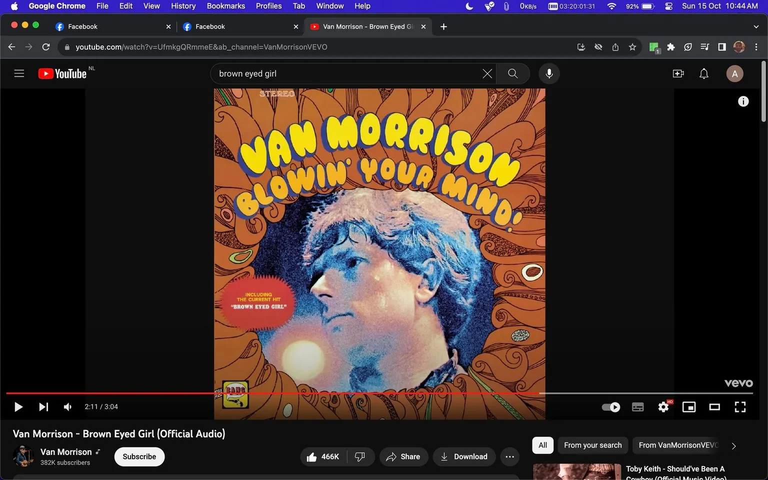 The screenshot depicts a YouTube page displaying the official audio for "Brown Eyed Girl" by Van Morrison. The main visual element is the album cover for "Blowin' Your Mind!" prominently featuring the name "Van Morrison" in bold yellow letters with a psychedelic design. The cover shows an artistic representation of Van Morrison's profile against a swirling, colorful background that captures the 1960s aesthetic. Below the image is text indicating the inclusion of the hit "Brown Eyed Girl."
The YouTube interface is visible with playback controls at the bottom. The video is paused at 2:11 of a total duration of 3:04. Other elements include a subscribe button, a like count with 466K likes, and options for sharing and downloading. The top of the screen shows a search bar with the query "brown eyed girl," and the tab indicates the use of Google Chrome. The video is hosted on the Van Morrison channel, which has 382K subscribers.