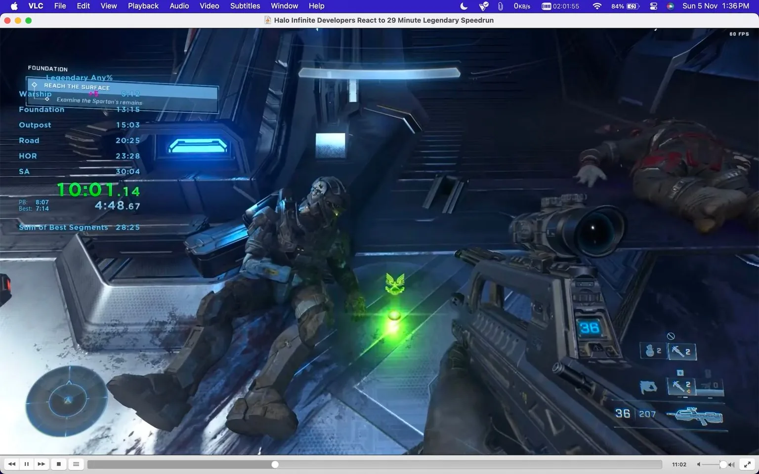 The screenshot shows a scene from the video game "Halo Infinite," specifically a first-person view within the game. The player is equipped with a futuristic weapon displaying the number 36 and other HUD elements, indicating ammunition and equipment. The scene is set in a sci-fi environment with sleek, metallic surfaces and blue lighting. A Spartan character is seen slumped against a wall, possibly deceased, with another body lying nearby. A glowing green item, resembling a small icon, is on the ground near the Spartan.
Text overlays indicate this is part of a speedrun attempt, with various time splits noted for sections like "Warship" and "Foundation," along with a current timer reading "10:01.14". The interface resembles VLC media player, with the window titled "Halo Infinite Developers React to 29 Minute Legendary Speedrun," implying the developers are reacting to a rapid completion of the game on a high difficulty setting. The layout includes playback controls and standard media player elements at the top and bottom of the frame.
- Title: "Halo Infinite Developers React to 29 Minute Legendary Speedrun"
- Site / app: "VLC"