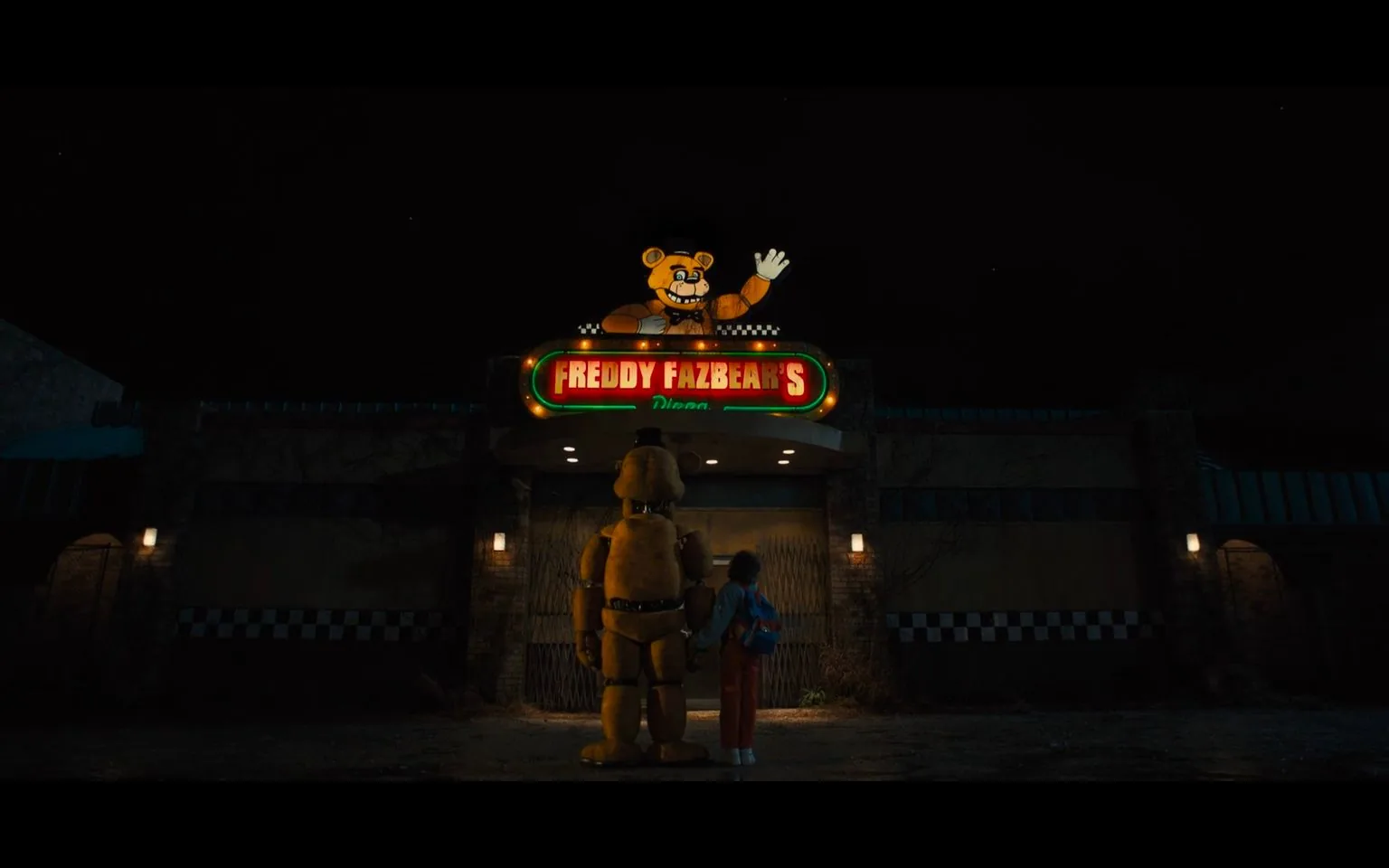 The image depicts a nighttime scene outside a building with a bright, colorful sign that reads "FREDDY FAZBEAR'S." Above the sign is a cartoonish bear mascot waving, which is consistent with the theme of the "Five Nights at Freddy's" franchise, known for its horror elements featuring animatronic characters.
In the foreground, an animatronic character, resembling a bear, stands next to a person. The animatronic is large, with a yellowish-brown color, and wears a black bowtie and top hat. The person beside it appears to be a young individual, wearing a blue jacket and red pants, with a backpack. They stand together facing the entrance, implying a moment of anticipation or curiosity.
The building's exterior is somewhat worn, with brick walls and checkerboard patterns, casting an eerie yet nostalgic ambiance. The lighting is dim, with only the sign and a few exterior lights illuminating the scene, enhancing the mysterious and suspenseful atmosphere typical of the "Five Nights at Freddy's" series.
