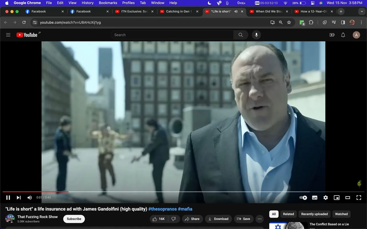 1) Rich description: The image captures a scene from a YouTube video titled "Life is short" a life insurance ad with James Gandolfini. The setting appears to be a cityscape, with tall buildings visible in the background, suggesting an urban environment. In the foreground, James Gandolfini is prominently featured. He is dressed in a dark suit with a light blue shirt, conveying a professional or serious demeanor. His expression is focused, and he appears to be addressing the camera directly. In the background, two other individuals are slightly blurred, seemingly engaged in a dramatic moment that contrasts with Gandolfini's composed presence. The lighting is bright, likely indicating a daytime scene. The composition and Gandolfini's attire suggest a formal advertisement tone. The video is hosted on the channel "That Fuzzing Rock Show," and the tags suggest themes related to "The Sopranos" and "mafia."
2) On-screen text block:
- Title: "\"Life is short\" a life insurance ad with James Gandolfini (high quality) #thesopranos #mafia"
- Channel / profile: "That Fuzzing Rock Show"
- Site / app: "YouTube"