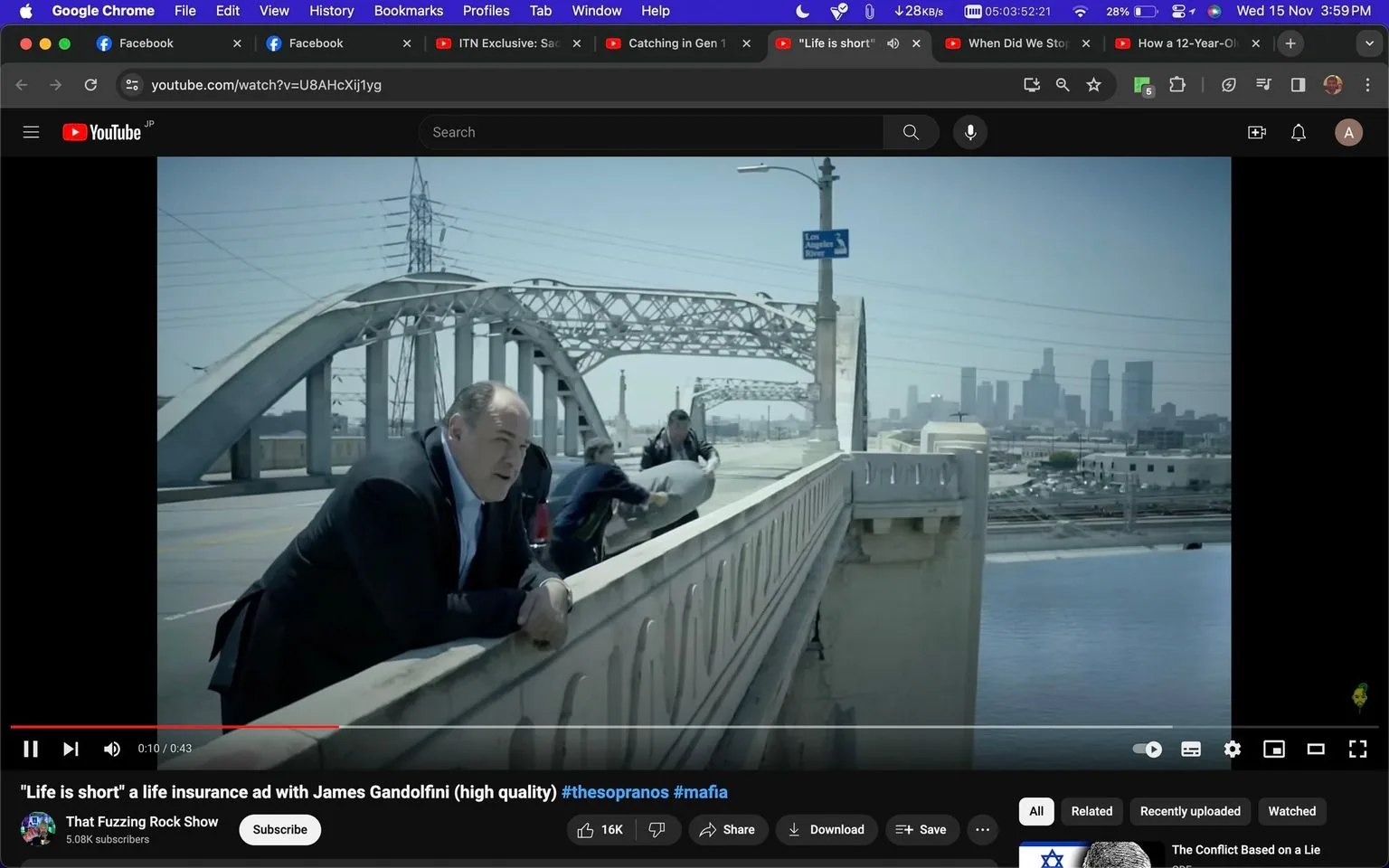 In this scene, James Gandolfini is shown leaning on a bridge railing, looking contemplative. The setting is an urban landscape, specifically the iconic Los Angeles bridge, with the city skyline visible in the background. The bridge features metal arches and a concrete barrier, typical of Los Angeles infrastructure. James Gandolfini is wearing a dark suit, which adds to the formal and somber mood of the scene. Two other people are in the scene, seemingly involved in moving an object, which adds a sense of activity and narrative depth.
The screenshot is from a YouTube video titled "\"Life is short\" a life insurance ad with James Gandolfini (high quality)," suggesting the thematic focus of the advertisement. The video is posted on a channel named "That Fuzzing Rock Show." The lighting is bright and clear, indicating daytime, which complements the serious but open atmosphere. There is a small sign that reads "Los Angeles," anchoring the setting geographically. The topic tags "#thesopranos" and "#mafia" suggest a connection to Gandolfini's well-known role in the television series "The Sopranos," adding context to his presence in the advertisement.