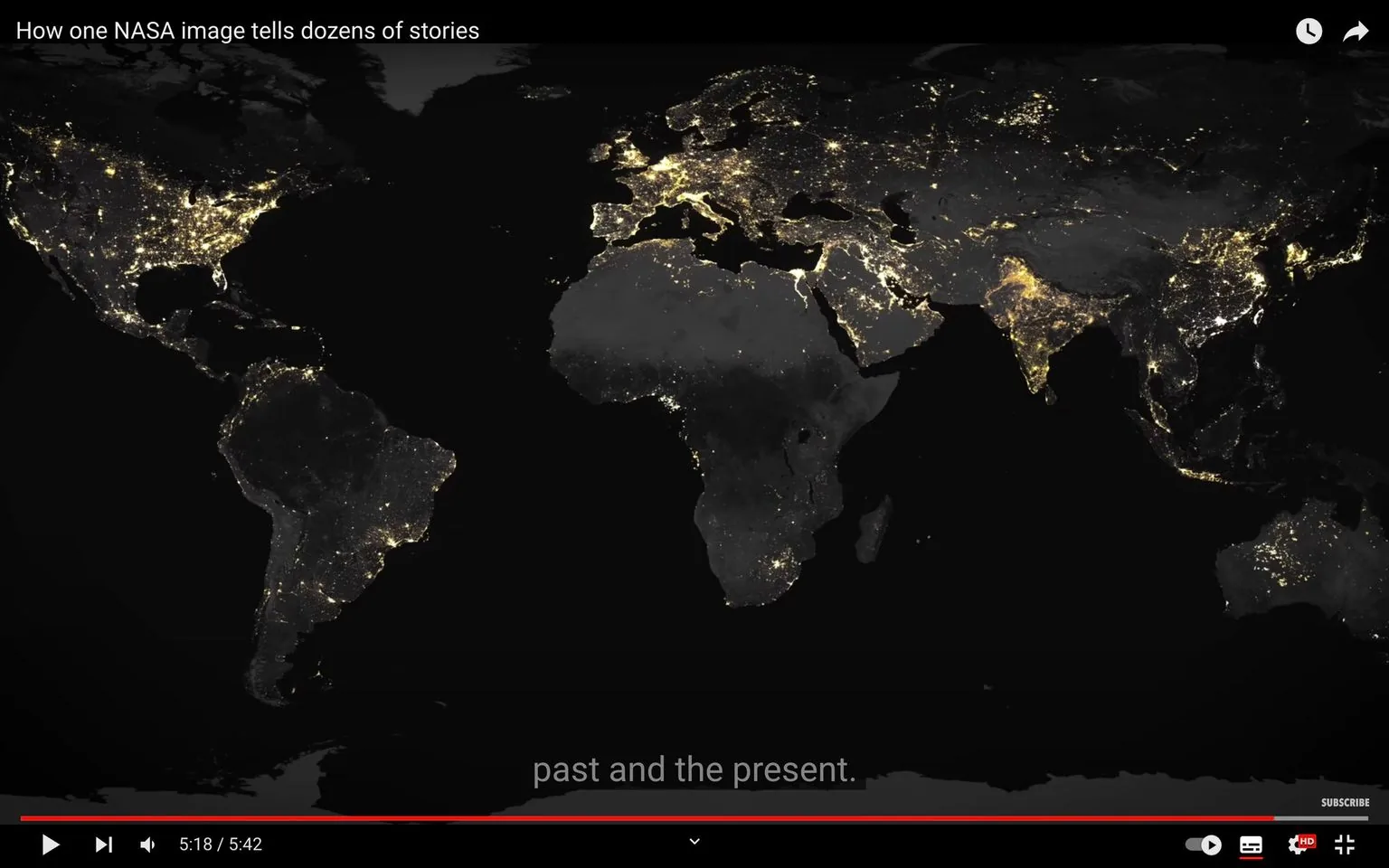 The image is a frame from a video titled "How one NASA image tells dozens of stories," sourced from YouTube. It showcases a global satellite view of Earth at night, highlighting the illuminated regions across different continents. The bright clusters of light indicate densely populated and urbanized areas, with noticeable concentrations in North America, Europe, and parts of Asia. This striking visual emphasizes the contrast between lit and unlit areas, suggesting differences in urban development and population density.
The frame includes a subtitle at the bottom, reading "past and the present." The dark and luminous sections create a compelling visual narrative about human settlement patterns and energy consumption. The map shows the continents in varying shades of black and gray, with the lights appearing in bright white or yellowish tones, illustrating the spread of artificial lighting. This image serves as a powerful representation of human activity as seen from space, capturing the interplay of light and darkness across the globe.