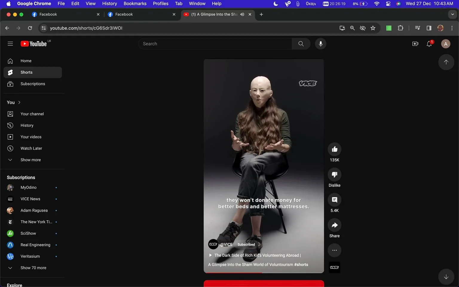The image is a screenshot from YouTube, displaying a short video by the channel @VICE. The video is titled "The Dark Side of Rich Kids Volunteering Abroad | A Glimpse Into the Sham World of Voluntourism #shorts." In the video frame, a person is seated on a stool against a dark grey background. They have long, wavy hair and are wearing a green long-sleeve top and dark pants. The lighting is focused on the individual, creating a stark contrast with the background. They are gesturing with their hands, indicating they might be explaining or discussing something important. The VICE logo is visible in the upper right corner, and overlay text reads, "they won't donate money for better beds and better mattresses." The video touches on themes related to voluntourism and its criticisms. The YouTube interface surrounds the video, showing interaction options like thumbs up and down, comment count, and share buttons. The browser tabs and address bar suggest this is viewed on Google Chrome.