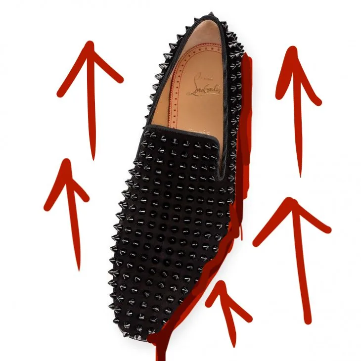 The image features a stylish black shoe adorned with an array of metal spikes, creating a striking and edgy appearance. The shoe is designed by the luxury brand Christian Louboutin, known for its distinctive red soles and high-end fashion items. The shoe is positioned against a white background, accentuated by hand-drawn red arrows pointing towards it, adding a bold and vibrant touch to the composition. The interior of the shoe reveals the brand's name, "Christian Louboutin," embossed on the tan leather lining. The overall mood is modern and luxurious, emphasizing the shoe's unique design and high-fashion appeal. This image likely aims to capture the attention of fashion enthusiasts and highlight the brand's creative and daring approach to footwear design.