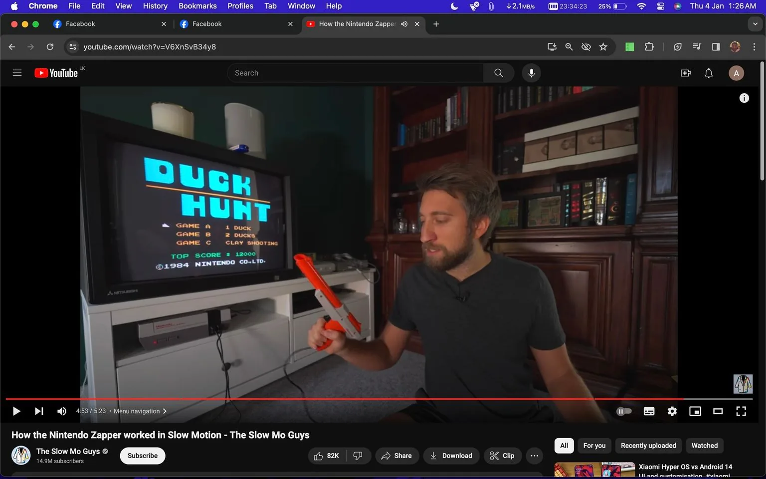 The image showcases a YouTube video titled "How the Nintendo Zapper worked in Slow Motion" by The Slow Mo Guys. The scene is set indoors with a cozy, library-like background featuring shelves filled with books. The focus is on a man from The Slow Mo Guys who is holding a classic Nintendo Zapper, a gray and orange light gun accessory for the Nintendo Entertainment System (NES). He appears to be explaining or demonstrating something, with a concentrated expression.
In the foreground is a CRT television displaying the title screen of the iconic game "Duck Hunt," which was released by Nintendo in 1984. The screen lists three game modes: "1 DUCK," "2 DUCKS," and "CLAY SHOOTING," along with a top score of 12000. Below the TV, an NES console is visible, adding to the nostalgic feel of the setting.
The lighting is warm, highlighting the retro gaming equipment and giving the room a comfortable ambiance. The presence of the Nintendo Zapper and "Duck Hunt" screen suggests the video is about demonstrating or exploring the workings of this classic gaming setup, possibly with slow motion technology, as indicated by the video title.
- Title: "How the Nintendo Zapper worked in Slow Motion - The Slow Mo Guys"
- Channel / profile: "The Slow Mo Guys"
- Site / app: "YouTube"