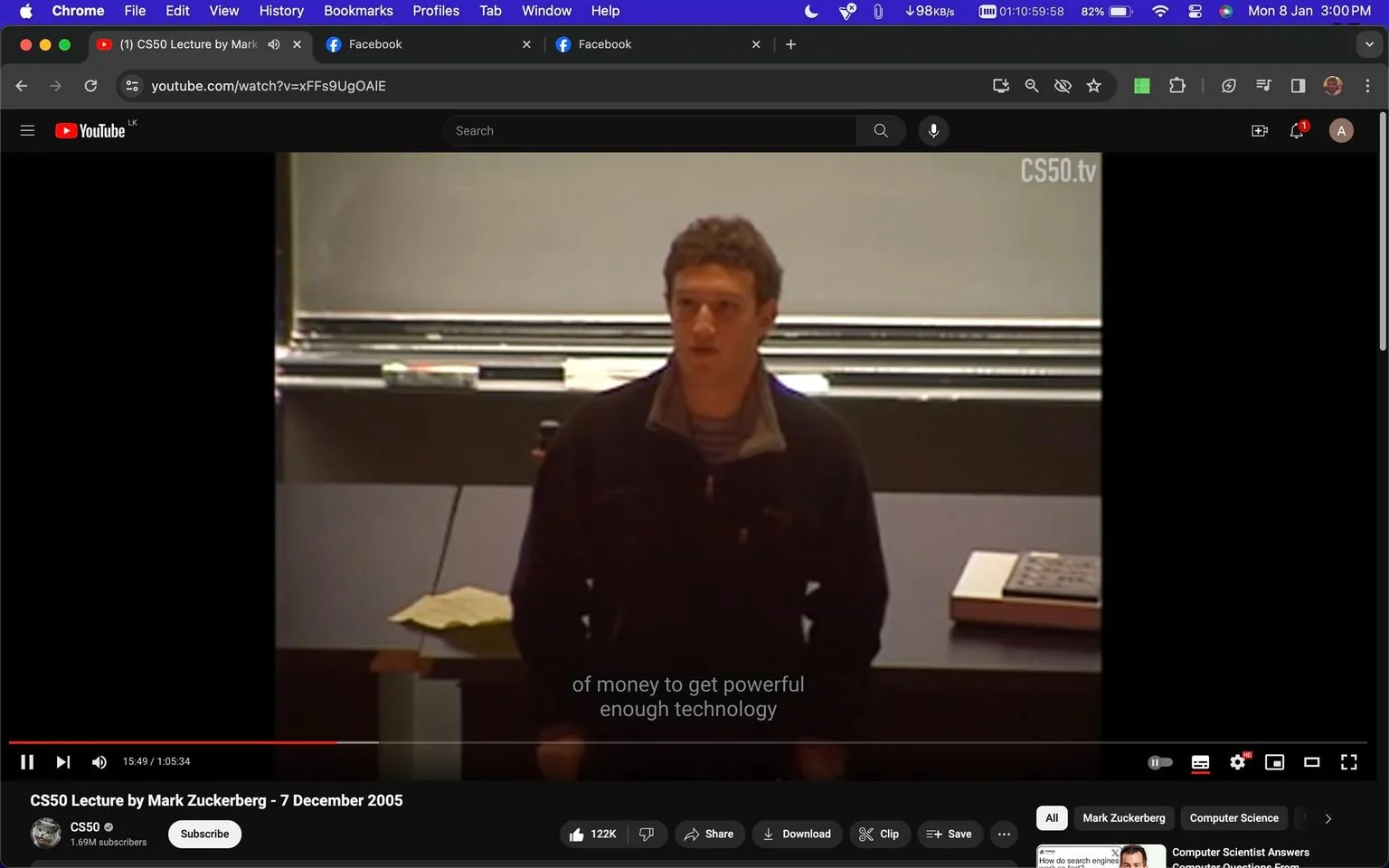 Mark Zuckerberg is pictured in a lecture setting, delivering a talk. The screenshot appears to be from a YouTube video titled "CS50 Lecture by Mark Zuckerberg - 7 December 2005," hosted on the CS50 channel. He is dressed casually, wearing a dark jacket and a striped shirt underneath. The setting is a traditional lecture hall, with a large blackboard behind him and a desk in front. A piece of paper is placed on the desk, and he seems to be engaged in a presentation, possibly discussing technology, as indicated by the subtitle: "of money to get powerful enough technology." The lighting is typical of an indoor environment, casting a warm tone over the scene. A small piece of text on the screen reads "CS50.tv." The lecture appears to focus on themes relevant to technology and education.