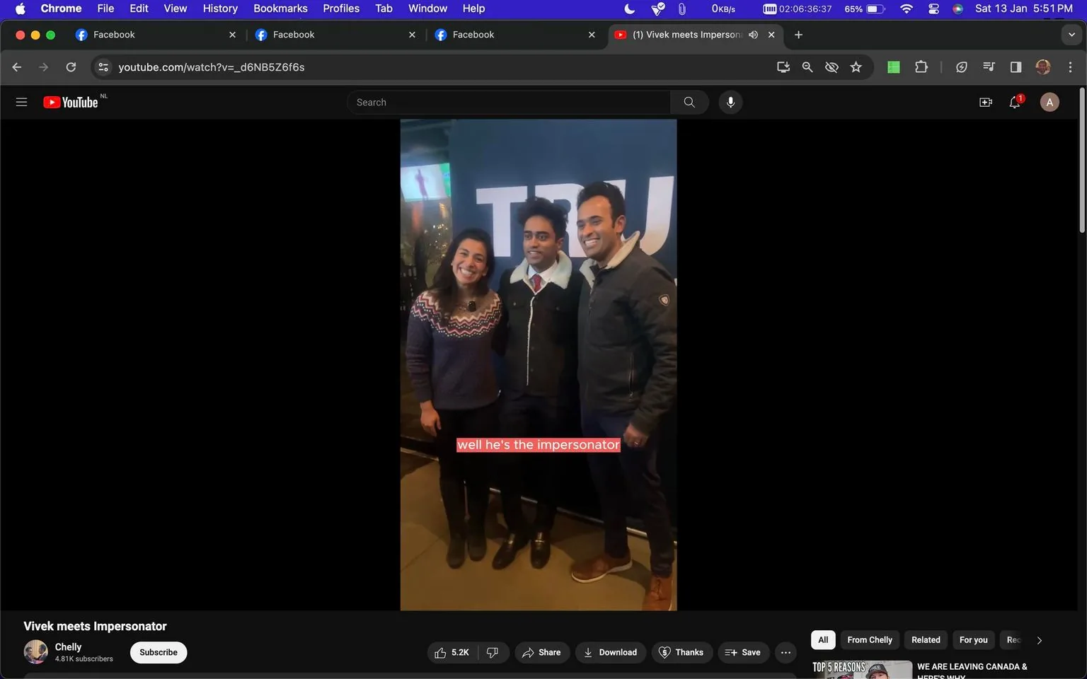 The image is a screenshot of a YouTube video titled "Vivek meets Impersonator" from the channel "Chelly." It shows three people standing indoors, posing for a photo. On the left is a woman wearing a dark blue sweater with a colorful pattern. In the middle is a man in a suit with a collared jacket, identified in the caption as the impersonator. On the right is another man wearing a dark jacket and brown shoes. The background features a large blue banner with partial text visible. The mood is friendly and casual, with all three individuals smiling. The video interface indicates standard YouTube features such as likes, share options, and the subscribe button. Captions at the bottom of the screenshot read, "well he's the impersonator." The setting suggests a social or event environment.