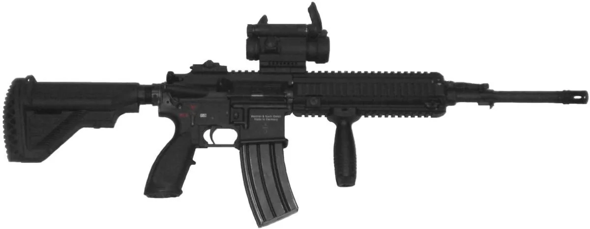 The image depicts a firearm, specifically a rifle, likely an HK416 model manufactured by Heckler & Koch. The weapon is shown in a side profile against a plain background, emphasizing its features. The rifle has a black finish and a tactical design with a number of components visible, including a collapsible stock, a vertical front grip, and a rail system on top and sides for mounting accessories. Attached to the top rail is a red dot sight, suggesting the weapon is outfitted for enhanced targeting.
The rifle's magazine is inserted, and its barrel extends to the right. The stock is adjustable, and the grip is ergonomic, designed for comfortable handling. The text "Heckler & Koch GmbH" and "Made in Germany" can be seen engraved on the side, indicating its manufacturer and origin. The image is likely taken indoors under controlled lighting, focusing on the rifle's details without any background distractions.