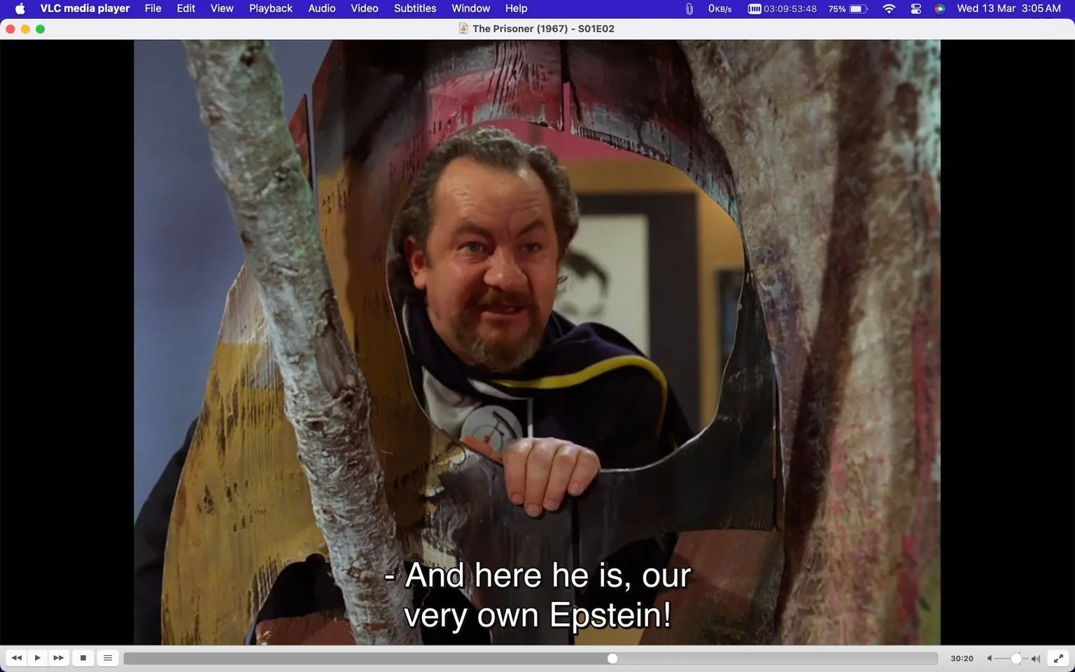 1) Rich description: The screenshot is from an episode of the television show "The Prisoner," specifically Season 1, Episode 2. Displayed within VLC media player, the scene shows a character peering through a circular opening in a wooden structure, with a playful and intrigued expression. The character is wearing a dark cloak with a yellow trim, suggesting a sense of role-play or theatricality. The setting is a colorful and abstract environment, possibly an art studio or a themed space, indicated by the vibrant backdrop and the makeshift structure. The lighting is bright, highlighting the character's face and emphasizing his animated expression. Subtitles at the bottom of the screen read, "- And here he is, our very own Epstein!" adding a humorous or ironic tone to the scene. The media player's interface is visible at the top and bottom, showing typical control buttons and menu options.
- Title: "The Prisoner (1967) - S01E02"
- Site / app: "VLC media player"
- Captions / subtitles: "- And here he is, our very own Epstein!"