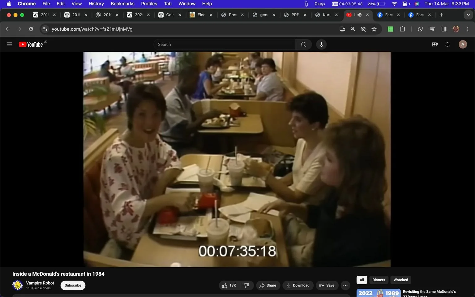 ```
The video frame captures a moment inside a McDonald's restaurant in 1984. Three people are seated at a table, enjoying their meal. The woman closest to the camera is wearing a white top with a red floral pattern and is engaged in a conversation. She appears cheerful and is gesturing slightly with her hands as if emphasizing a point. The two other women at the table are listening attentively; one is wearing a white top and the other a dark-colored outfit. The table is laden with typical fast-food items: a burger, fries in the iconic red McDonald's packaging, and drinks with straws.
The setting is warm and nostalgic, characteristic of 1980s interior design, evident in the wooden booth seating and simple decor. In the background, other patrons are visible, suggesting a busy lunchtime environment. Bright natural light filters in from the windows, creating a lively and inviting atmosphere. The timestamp "00:07:35:18" is visible on the screen, indicating the video’s runtime. The video is hosted on YouTube under the channel "Vampire Robot," which often revisits historical or vintage themes.