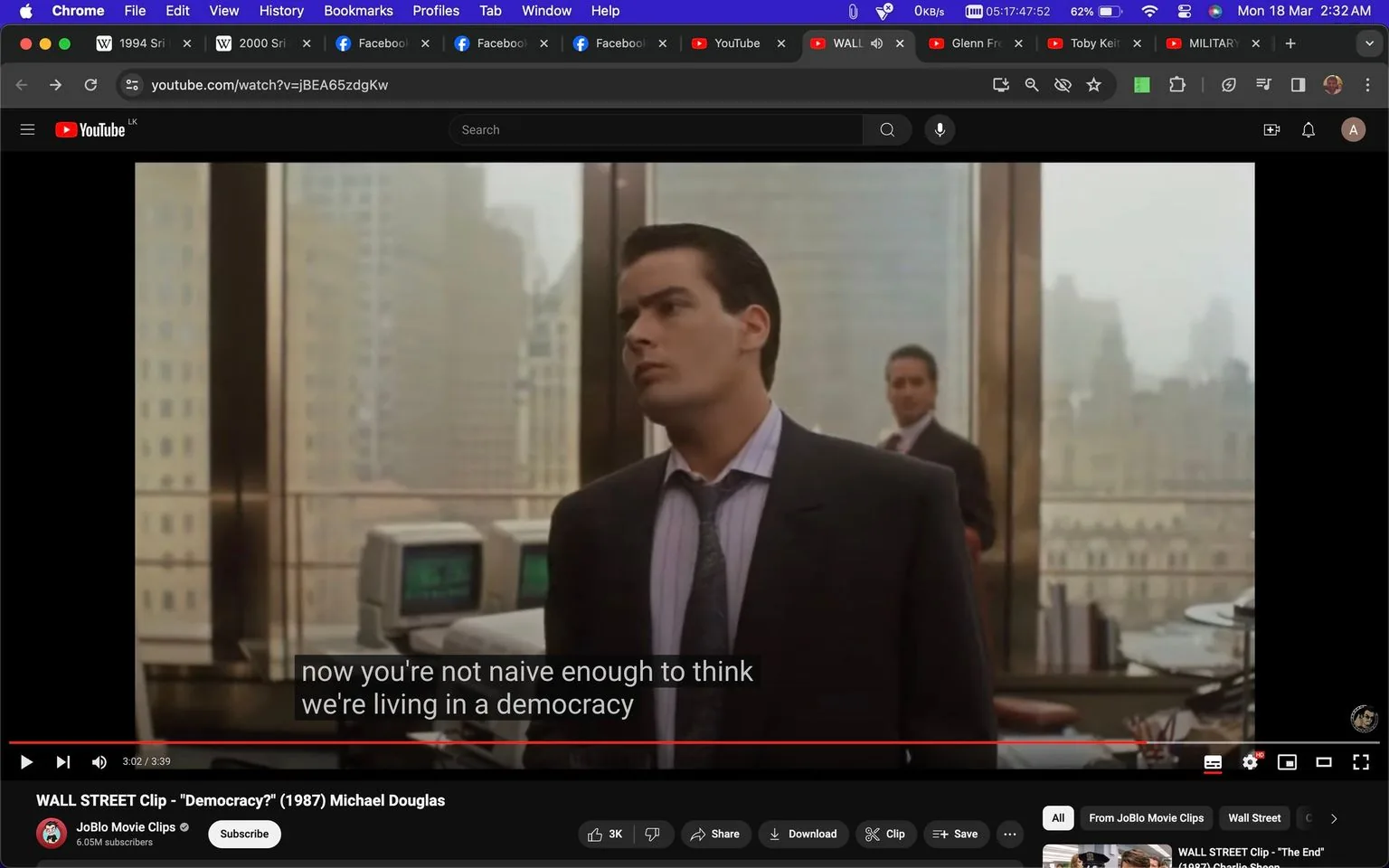 The image is a screenshot from a YouTube video titled "WALL STREET Clip - \"Democracy?\" (1987) Michael Douglas" on the channel JoBlo Movie Clips. The scene is from the movie "Wall Street," featuring Charlie Sheen. He is in an office setting, wearing a dark suit with a striped shirt and a tie. His expression appears contemplative or skeptical, as he looks slightly to the side. The office has large windows with a cityscape view in the background, and there are old-style computer monitors visible on a desk. The lighting is soft, typical of an indoor scene during the day. The subtitle reads, "now you're not naive enough to think we're living in a democracy," indicating a conversation about political or social themes. The setting and attire suggest a professional environment, possibly indicating a business meeting or a significant dialogue in the film.
- Title: "WALL STREET Clip - \"Democracy?\" (1987) Michael Douglas"
- Channel / profile: "JoBlo Movie Clips"
- Site / app: "YouTube"
- Captions / subtitles: "now you're not naive enough to think we're living in a democracy"