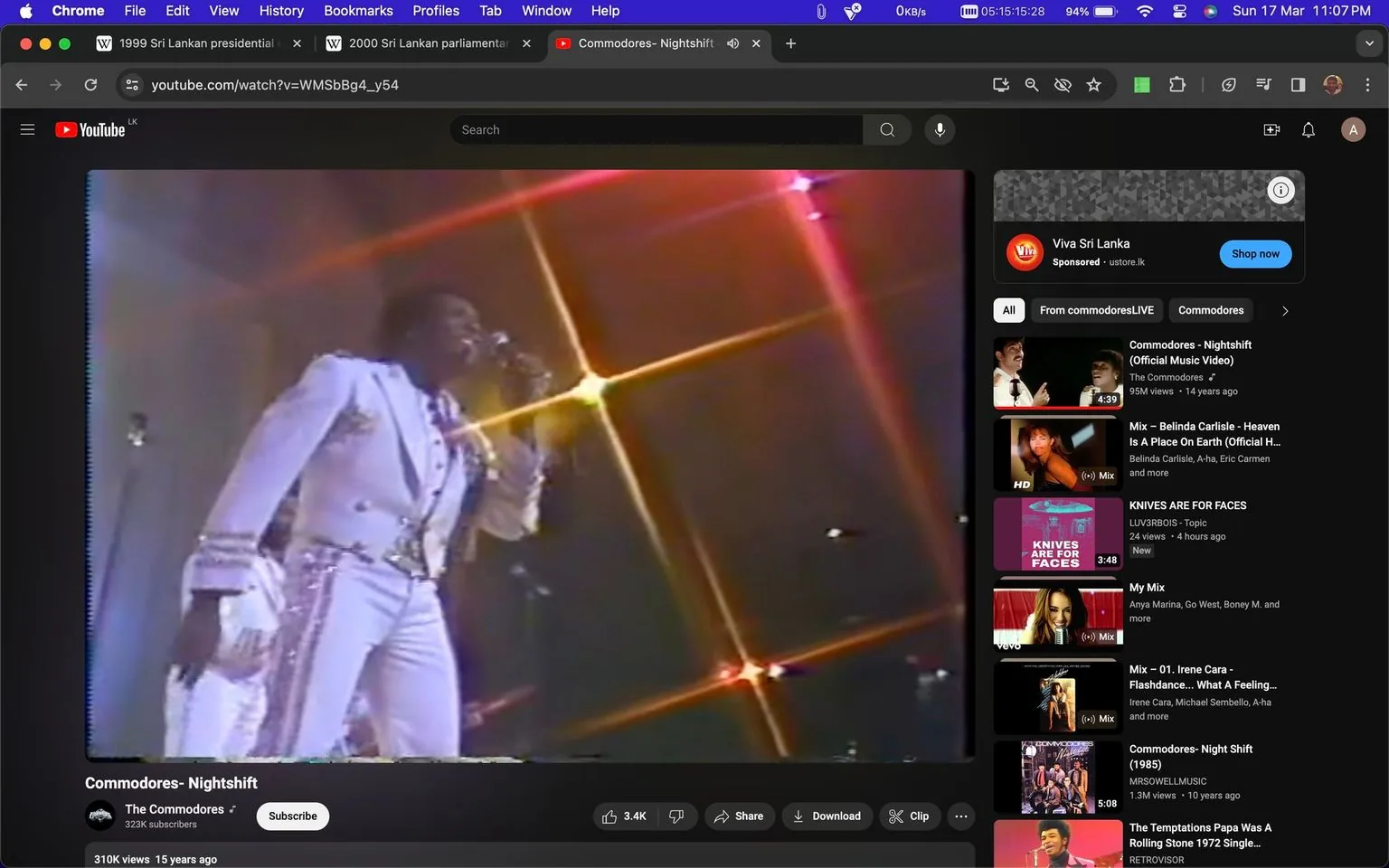 The image is a screenshot from a YouTube video titled "Commodores- Nightshift," performed by The Commodores. The video presents a live performance, with a singer on stage wearing an elaborate white suit adorned with glittering details, typical of a showman's outfit. The lighting is vibrant, with lens flares creating a dynamic atmosphere, adding to the energy of the live concert setting. The screenshot captures the excitement of a live music performance, with the artist engaged with the microphone, suggesting they are mid-song. The video is uploaded on the channel "The Commodores" and has garnered 310K views, indicating its popularity. Various suggested videos related to music are visible on the right side, enhancing the context of this being a music-focused content platform. The overall mood of the scene is lively and engaging, capturing the essence of a live performance.
- Title: "Commodores- Nightshift"
- Channel / profile: "The Commodores"
- Site / app: "YouTube"