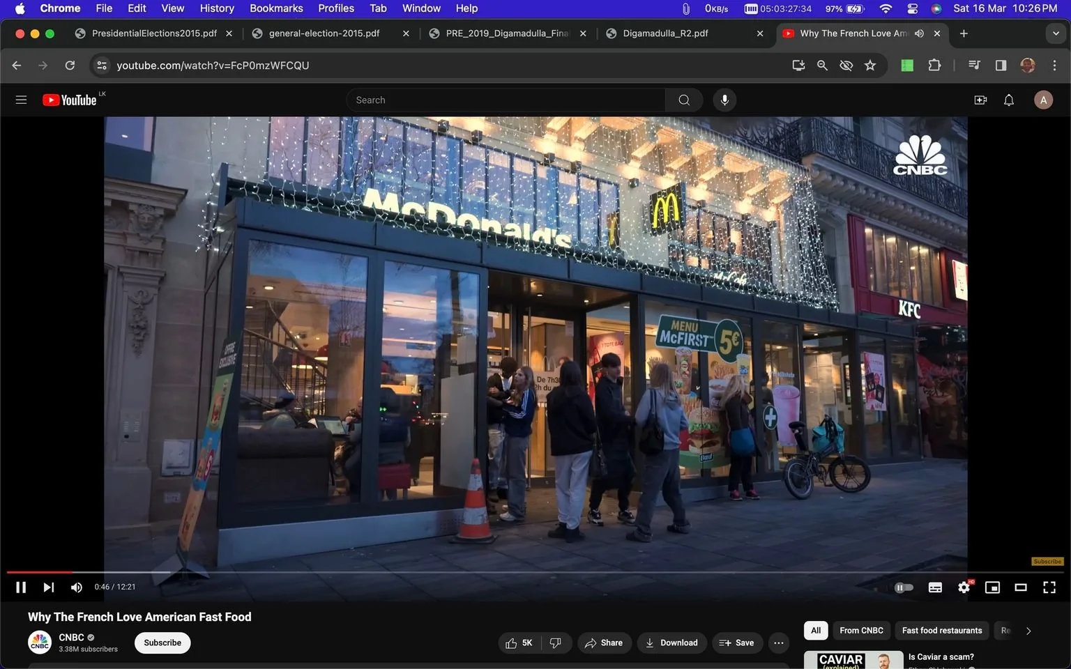 The screenshot captures a YouTube video titled "Why The French Love American Fast Food" by CNBC. The scene is set outside a McDonald's restaurant, adorned with decorative lights, suggesting a festive or evening setting. Several people are gathered at the entrance, indicating it might be a busy time. The McDonald's logo is prominently displayed above the entrance, with a sign advertising a "MENU McFIRST" for 5€. Adjacent to McDonald's is another fast-food chain, KFC, visible in the background. The atmosphere conveys a lively urban environment with a mix of casual attire among the patrons. The storefronts are well-lit, contrasting against the dimming evening light, creating an inviting ambiance. This scene suggests a discussion of the popularity and cultural impact of American fast food in France.
- Title: "Why The French Love American Fast Food"
- Channel / profile: "CNBC"
- Site / app: "YouTube"