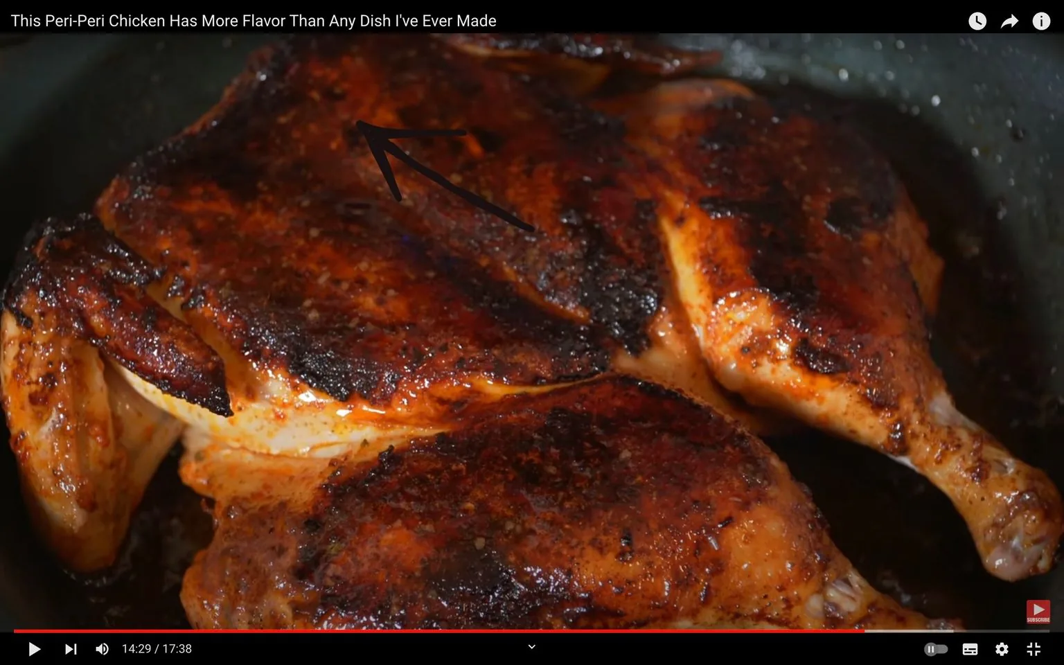 The image is a video frame showcasing a dish of Peri-Peri chicken. The chicken appears to be cooked to perfection, with a rich, dark, crispy skin indicating a well-seasoned and possibly spicy flavor profile. The chicken's golden brown color is enhanced by a layer of spices, which seem to give it a caramelized crust. The dish is prominently featured in the foreground, occupying most of the frame, suggesting it is the centerpiece of the video. The background is blurred, focusing the viewer's attention entirely on the chicken. An arrow drawn on the image points to a specific part of the chicken, likely highlighting a feature or technique being discussed in the video. The lighting is natural and warm, which enhances the appetizing appearance of the dish. The title of the video at the top reads, "This Peri-Peri Chicken Has More Flavor Than Any Dish I've Ever Made," indicating a personal endorsement of the dish's taste. The video seems to be part of a culinary channel or series focusing on flavorful recipes.