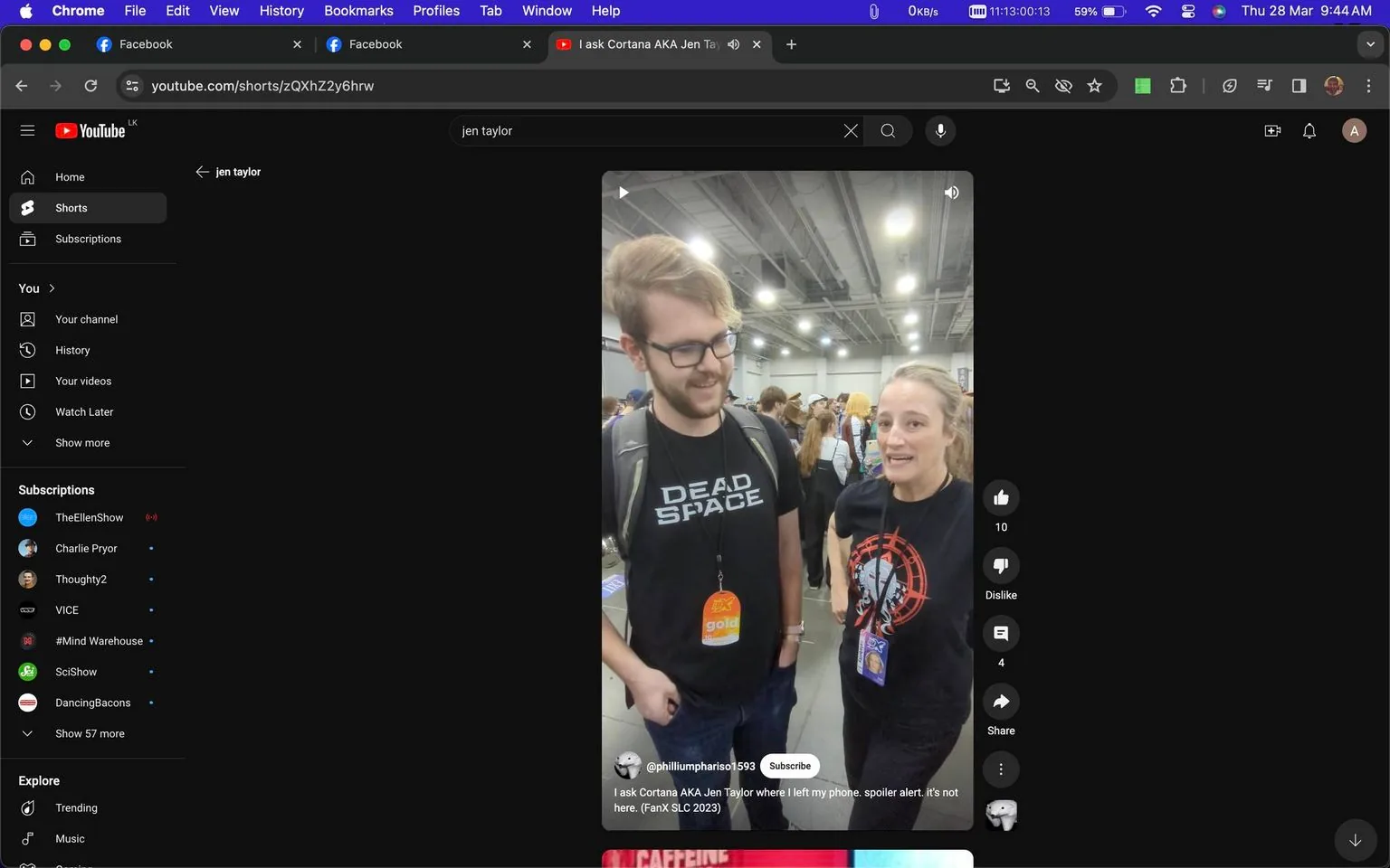 In this YouTube screenshot, two individuals are captured in a lively indoor convention setting, likely FanX SLC 2023. The person on the right is identified as Jen Taylor, known for her role in "Halo 3." She is wearing a black t-shirt with a red and white design, standing in a casual conversational pose with a friendly expression. The individual to her left is wearing a black "Dead Space" t-shirt and a lanyard with a badge that reads "gold," suggesting they might be an event attendee. The setting is bustling with people in the background, under bright, even lighting, typical of a convention hall. The screenshot is from a YouTube short titled "I ask Cortana AKA Jen Taylor where I left my phone. spoiler alert. it’s not here." The channel associated with this content is "@philliumphariso1593." The atmosphere is casual and engaging, reflecting the informal interactions typical at fan conventions.