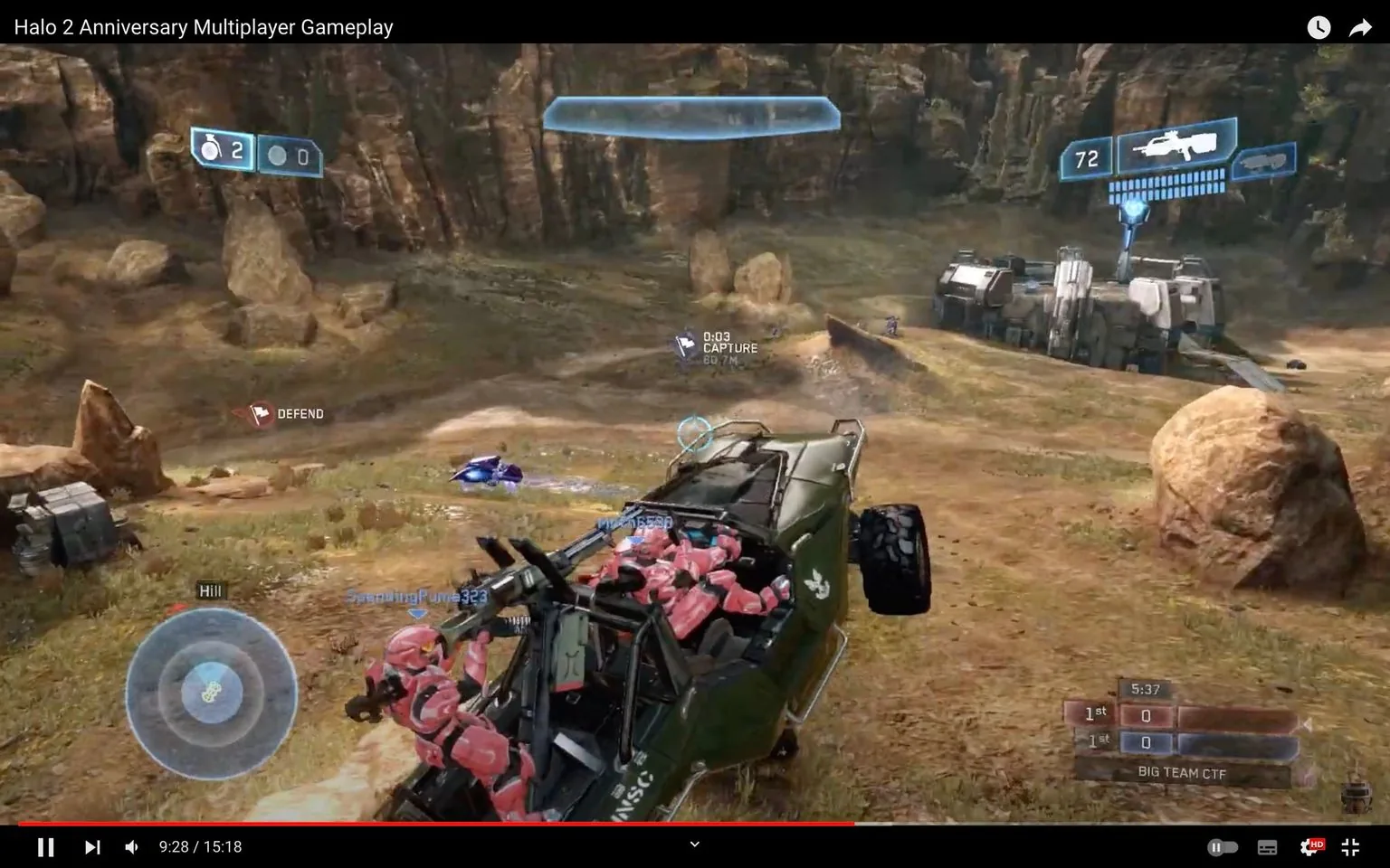 1) Rich description: This image is a frame from a gameplay video titled "Halo 2 Anniversary Multiplayer Gameplay." The scene is set in an outdoor environment with rocky terrain and sparse vegetation. In the foreground, a green Warthog vehicle is prominently featured, carrying characters dressed in pink armor. These characters are likely players in a multiplayer match of the game "Halo." The vehicle is positioned at an angle, suggesting motion or an active engagement in the game. In the background, a building structure is visible, set against a backdrop of rocky cliffs. On-screen text displays gameplay objectives such as "DEFEND" and "CAPTURE," along with a radar indicating player positioning. The heads-up display shows weapon and vehicle statistics, typical of a first-person shooter interface. The lighting appears natural, indicating a daytime setting within the game.
2) On-screen text block:
- Title: "Halo 2 Anniversary Multiplayer Gameplay"