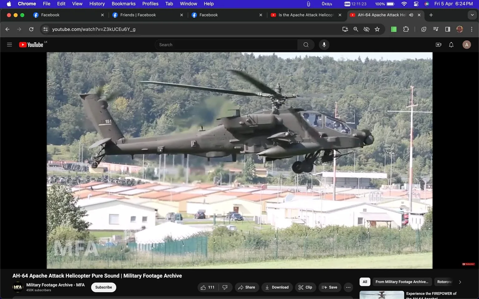 The screenshot captures a YouTube video titled "AH-64 Apache Attack Helicopter Pure Sound | Military Footage Archive." It features an Apache AH64 gunship, a military helicopter known for its combat capabilities. The helicopter is flying low over a landscape with a backdrop of dense trees and several buildings, likely part of a military base or installation. The AH64 is depicted in mid-flight, showing its distinctive twin rotors and armed configuration, which includes missile launchers and machine guns. The image is taken during the day with clear skies, providing a well-lit view of the helicopter's details.
The YouTube channel "Military Footage Archive - MFA," with 450K subscribers, is visible in the bottom portion of the screen, along with various user interface elements like the like, share, and save buttons. Other browser tabs suggest a focus on social media and video content. The scene conveys a sense of precision and military prowess, capturing the helicopter in a moment of dynamic motion. The overall mood is serious and focused, emphasizing the technical and strategic aspects of military aviation. The layout includes multiple tabs indicative of typical browsing activity, with a Facebook tab visible alongside the YouTube video.