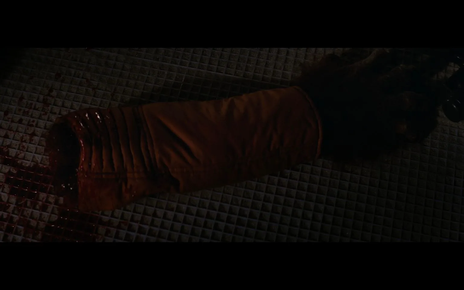 The image is a dramatic and dark scene from "Star Wars." It captures a severed arm, clad in an orange sleeve, lying on a grid-patterned floor. The arm appears to be covered in fur, suggesting it may belong to a non-human character from the "Star Wars" universe. Blood is visible near the severed end of the arm, adding to the intensity of the scene. The lighting is dim, emphasizing the somber and dramatic mood typical of many action-packed moments in "Star Wars" films. The choice of costume and special effects reflects the film’s commitment to detailed and immersive storytelling, characteristic of the "Star Wars" series. The setting appears to be indoors, possibly within a spaceship or a space station, enhancing the science fiction theme of the franchise. The overall composition is designed to evoke a strong emotional response, drawing viewers deeper into the narrative, highlighting the stakes and conflicts faced by the characters in this iconic series.