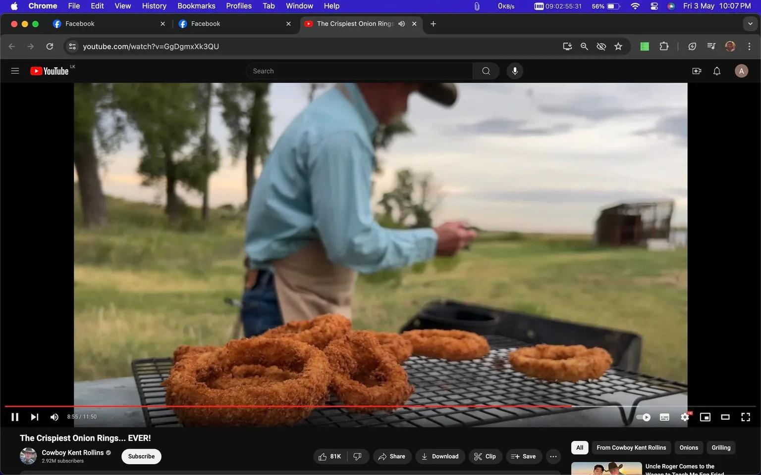 In this screenshot from a YouTube video titled "The Crispiest Onion Rings… EVER!", the scene captures a rustic outdoor setting. The focus is on a pile of crispy onion rings placed on a metal rack, suggesting they have just been freshly fried. The foreground is dominated by the golden-brown onion rings, emphasizing their crunchy texture. Slightly blurred in the background, a person—presumably Cowboy Kent Rollins—wears a light blue shirt, jeans, and a cowboy hat, embodying a quintessential Western look. He seems to be preparing or handling something out of focus, perhaps related to the cooking process. The surrounding environment includes grassy fields and distant trees, adding to the rustic and natural ambiance. The lighting is soft, with a slightly overcast sky visible, indicating an early morning or late afternoon setting.
- Title: "The Crispiest Onion Rings… EVER!"
- Channel / profile: "Cowboy Kent Rollins"
- Site / app: "YouTube"