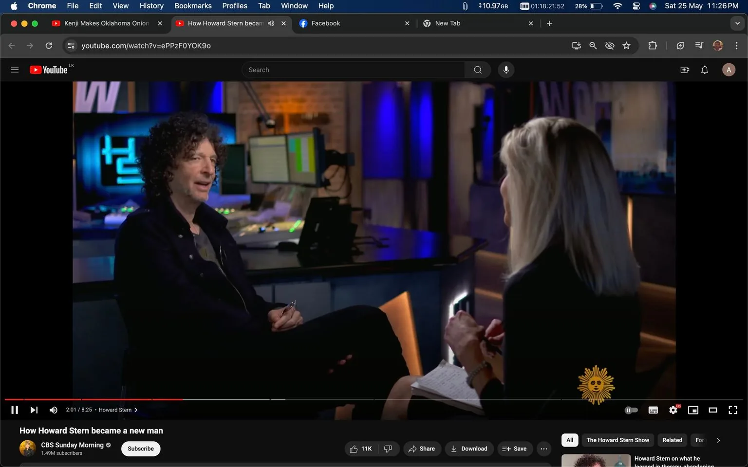 The image is a screenshot from a YouTube video titled "How Howard Stern became a new man," which is available on the "CBS Sunday Morning" channel. The scene is set in an indoor studio environment where an interview is taking place. Howard Stern is seated on the left, dressed in a dark jacket with a casual shirt underneath. He appears engaged and is holding a pen, suggesting he might be taking notes or emphasizing a point. The interviewer, a woman with long blonde hair, is seated on the right, facing Stern. She is holding a notepad, indicating a formal interview setting.
The studio is softly lit with blue and warm tones, creating an inviting atmosphere. Behind Stern, there are multiple monitors and radio equipment, reflecting the professional setup typical of a broadcast studio. The prominent use of blue lighting adds a modern and sleek aesthetic to the scene. The overall mood is professional yet relaxed, with both parties appearing focused and attentive. The setting and attire suggest a structured and serious interview, likely discussing personal or professional aspects of Howard Stern's life.