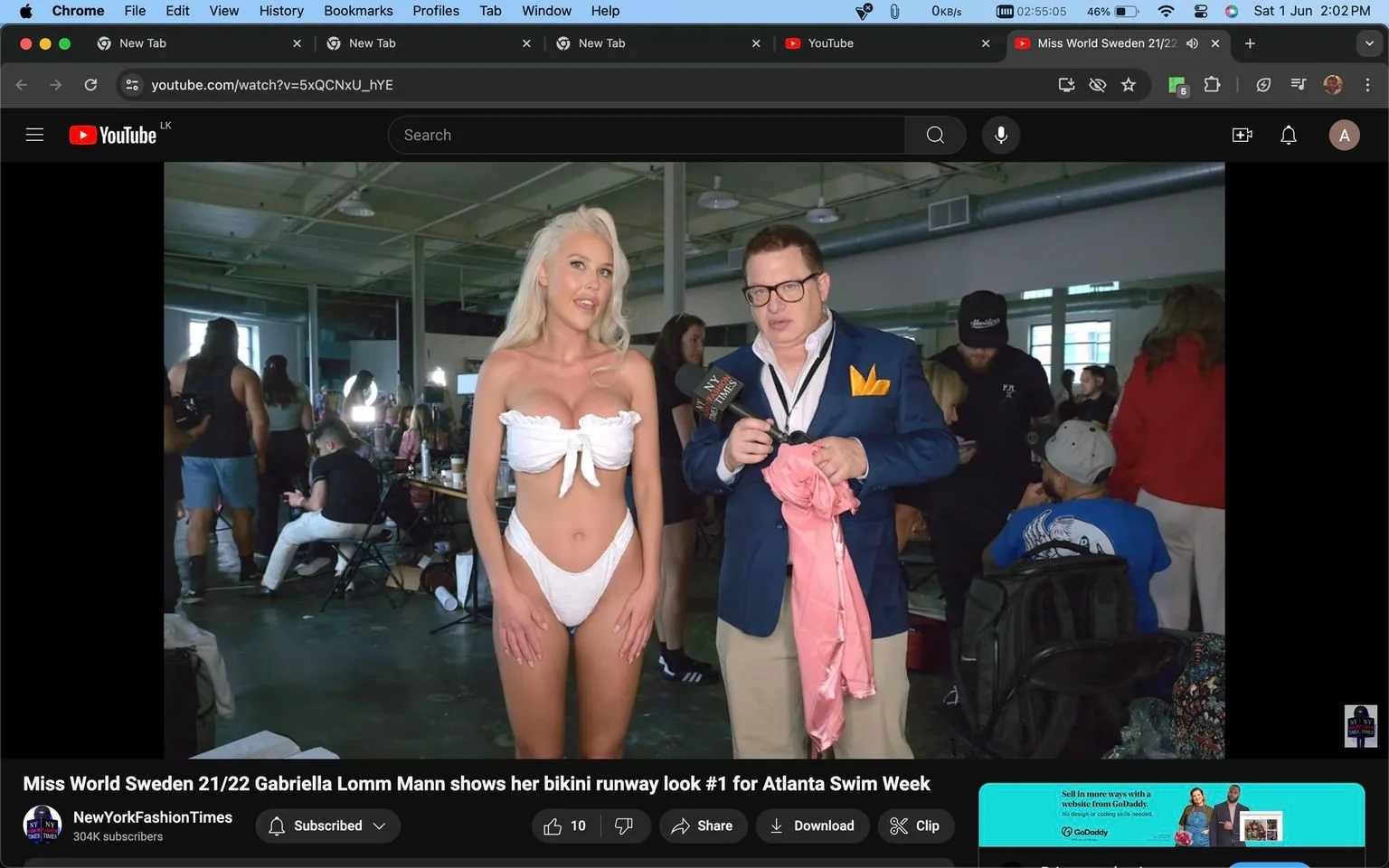 1) This image is a video frame from a YouTube video titled "Miss World Sweden 21/22 Gabriella Lomm Mann shows her bikini runway look #1 for Atlanta Swim Week," published by the channel NewYorkFashionTimes. The setting is an indoor space, likely backstage at a fashion event, given the presence of models and photographers. In the foreground, a woman stands confidently, wearing a white bikini with a bow design, indicative of a swimwear fashion context. Beside her is a man, identified in the hint as Peter Ronen, dressed in a dark blue blazer with a yellow pocket square, holding a microphone labeled with "NYFTV," suggesting an interview or coverage of the event. The background is bustling with people, some seated and others standing, indicative of the preparations for a fashion show. The lighting is bright, typical of indoor settings, highlighting the vibrant atmosphere of the event.
2) On-screen text block:
- Title: "Miss World Sweden 21/22 Gabriella Lomm Mann shows her bikini runway look #1 for Atlanta Swim Week"
- Channel / profile: "NewYorkFashionTimes"
- Site / app: "YouTube"