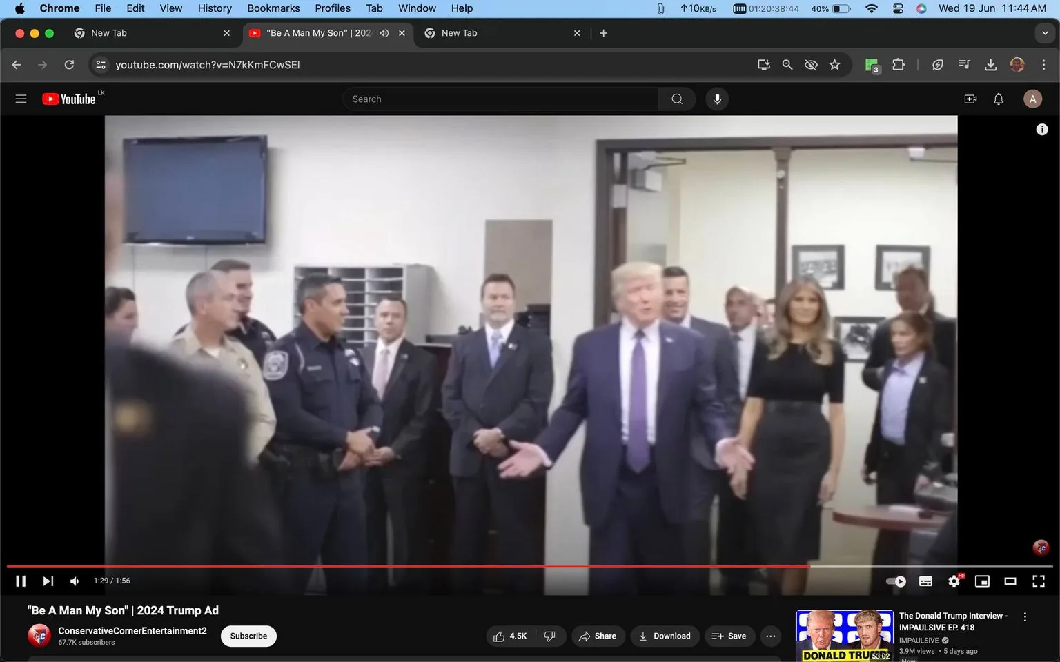 The image is a screenshot from a YouTube video titled "\"Be A Man My Son\" | 2024 Trump Ad," uploaded by the channel "ConservativeCornerEntertainment2". The scene takes place indoors, likely in an official or professional setting, such as a government office or conference room. Donald Trump is at the center of the image, gesturing with his hands, indicating he is speaking or addressing the group. Melania Trump is to his side, wearing a black dress, standing calmly.
A group of people, including law enforcement officers in uniform and men in suits, are gathered around, paying attention to Trump. The environment is formal, with neutral-colored walls, a television mounted in the background, and framed photographs or documents on the walls, contributing to the official ambiance. The lighting is bright, typical of indoor settings with overhead lighting, and everyone appears focused or engaged with the scene. The video's context points towards political themes, potentially related to an upcoming election.