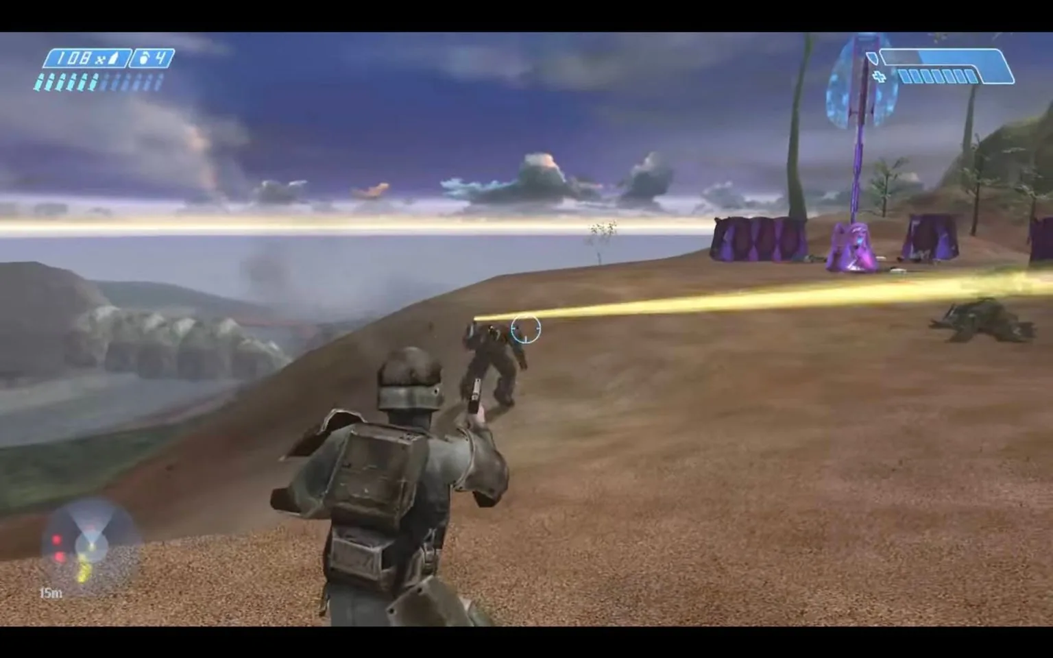 This image is a screenshot from the video game "Halo: Combat Evolved." It showcases a first-person shooter perspective, where the player character, a soldier in futuristic armor, is engaged in combat on a sandy, open terrain. The soldier is aiming a weapon at an enemy in front of him, who appears to be firing back, indicated by a bright yellow beam of light. In the background, there are purple alien structures typical of the Halo universe, and the landscape extends to a horizon featuring mountains and a body of water under a partly cloudy sky. The display on the top left corner shows the player's health and ammo status, while a minimap is visible in the bottom left corner. The overall atmosphere is tense, with a focus on action and sci-fi elements, emphasized by the distinctive color palette and design of the game world.