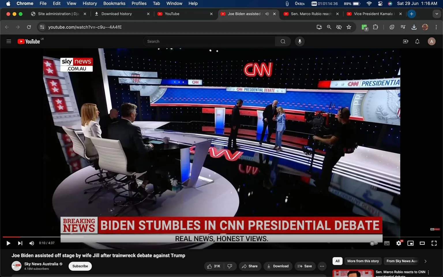 The screenshot captures a moment from a televised event, specifically a CNN presidential debate stage. The setting is a well-lit studio with a modern design, featuring a prominent CNN logo and an American-themed backdrop with stars and stripes. On stage, a tall man is assisted by a woman, both identified in the hint as Joe Biden and his wife Jill. Joe Biden appears to be leaving the stage with Jill's support, while a camera operator in the foreground captures the scene.
Seated at a curved desk in the left foreground are two individuals, likely news commentators, observing the unfolding events. The desk is sleek and modern, and the studio lighting is bright, creating a professional atmosphere. The color scheme is predominantly blue and red, matching the theme of a U.S. presidential debate.
Text on the screen reads "BIDEN STUMBLES IN CNN PRESIDENTIAL DEBATE" and "REAL NEWS, HONEST VIEWS," alongside the Sky News Australia logo. This suggests the broadcast is from Sky News, covering the debate's aftermath. The YouTube title indicates that Joe Biden needed assistance from his wife Jill after a challenging debate against Trump. The studio is bustling with activity, indicative of the high-stakes nature of the event.
- Title: "Joe Biden assisted off stage by wife Jill after trainwreck debate against Trump"
- Channel / profile: "Sky News Australia"
- Site / app: "YouTube"