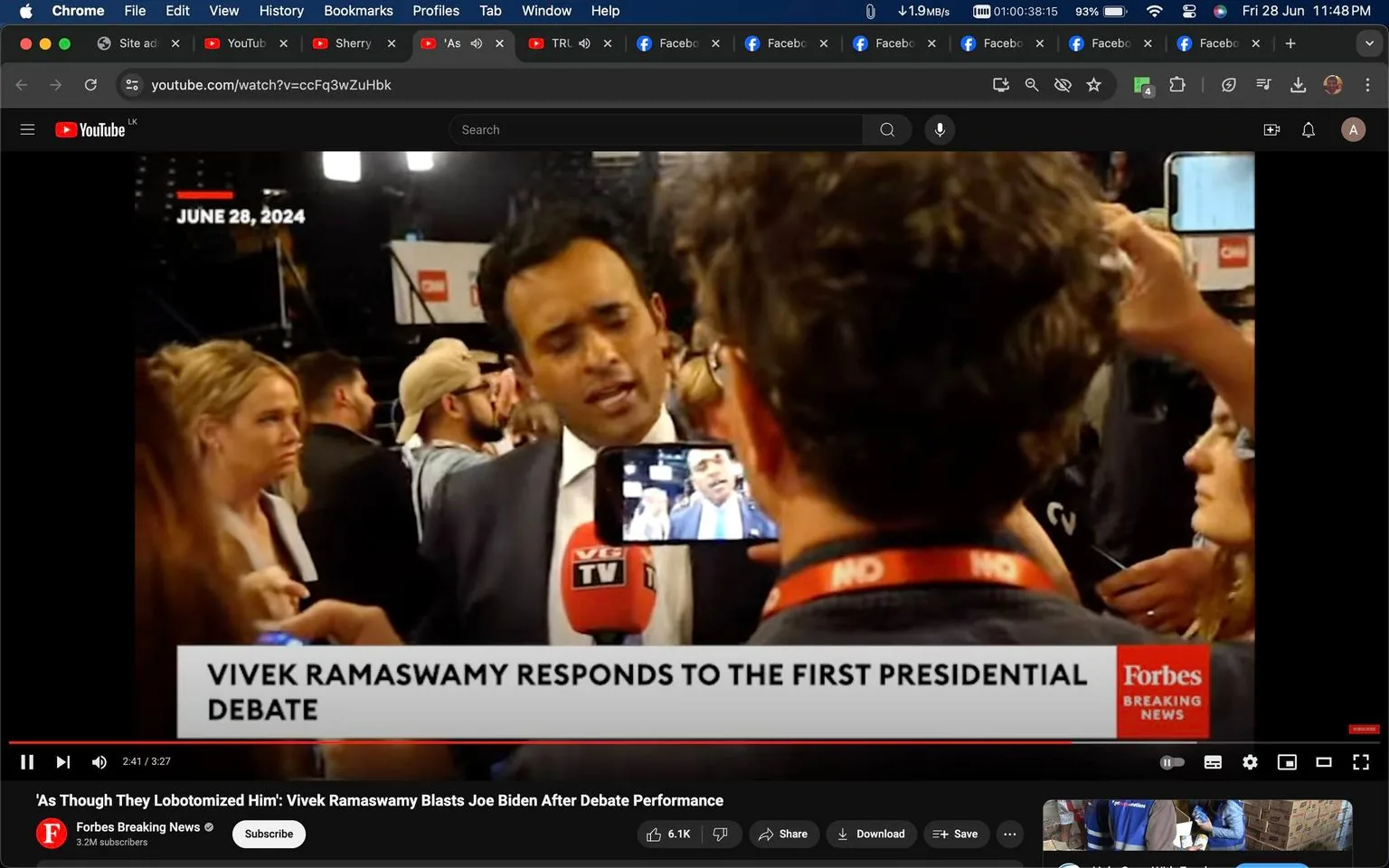 The image is a screenshot from a YouTube video titled "'As Though They Lobotomized Him': Vivek Ramaswamy Blasts Joe Biden After Debate Performance," hosted on the Forbes Breaking News channel. The setting is an indoor press area with Vivek Ramaswamy speaking to reporters after the first presidential debate. It is dated June 28, 2024.
Vivek Ramaswamy is central in the frame, being interviewed by multiple journalists. He is dressed in a suit, holding a VGTV-branded microphone. A smartphone in the foreground captures his image as he speaks, indicating a lively media environment. The background shows other attendees and a CNN logo, highlighting the event's high-profile nature. The mood is serious yet energetic, as journalists focus on Ramaswamy's responses. The lighting is bright, typical of press gatherings, emphasizing the significance of the occasion. The on-screen text mentions the date and that Ramaswamy is responding to the debate.