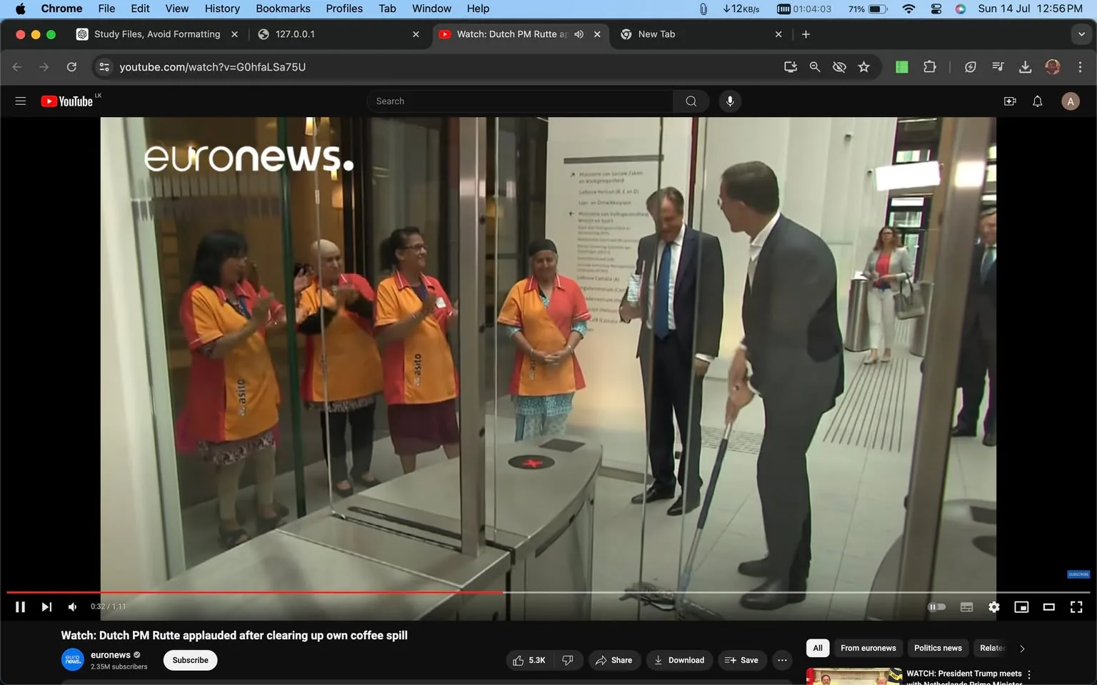 The image is a screenshot from a YouTube video titled "Watch: Dutch PM Rutte applauded after clearing up own coffee spill," posted by the channel "euronews." It shows a scene inside an office building, where a man in a suit, identified as Dutch PM Rutte, is mopping the floor. He is surrounded by a group of people, some of whom appear to be cleaning staff, wearing orange and red uniforms. They are standing to the side, clapping and smiling, indicating appreciation for his actions. The interior setting is modern with glass partitions and a light color scheme. In the background, a few other people in professional attire are observing the scene. The atmosphere is positive and respectful, highlighting an act of humility from a public figure. The composition includes branding from "euronews" in the top left corner and some visible text on a wall sign.
