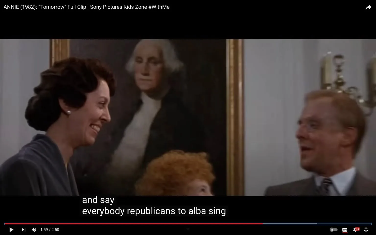 The image is a frame from the movie "Annie" (1982), shared on the Sony Pictures Kids Zone YouTube channel. It features a scene set indoors with a prominent portrait of George Washington painted by Gilbert Charles Stuart in the background. The scene captures two adults in conversation, both smiling, with one woman dressed in a dark suit and a man in a suit and tie. The lighting is soft, focusing on the subjects and the historical painting behind them. A young girl with curly red hair can be seen partially between the two adults, suggesting a lively, engaging moment. The subtitle at the bottom, "and say everybody republicans to alba sing," adds a humorous, if slightly confusing, touch to the scene. The composition draws attention to the mix of historical and contemporary elements, providing a warm and nostalgic atmosphere typical of the film's setting.
- Title: "ANNIE (1982): “Tomorrow” Full Clip | Sony Pictures Kids Zone #WithMe"
- Channel / profile: "Sony Pictures Kids Zone"
- Site / app: "YouTube"
- Captions / subtitles: "and say", "everybody republicans to alba sing"
