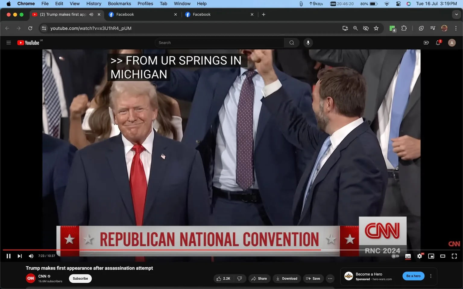 The image is a video frame from a YouTube video titled "Trump makes first appearance after assassination attempt" on the CNN channel. It shows a scene at the Republican National Convention with a focus on a man, hinted to be Trump, wearing a dark suit, white shirt, and red tie. He is standing with a slight smile on his face, surrounded by other individuals in suits. The setting appears lively, with people in the background showing enthusiasm, as indicated by raised arms and gestures. The caption on the screen reads "FROM UR SPRINGS IN MICHIGAN," suggesting a specific location or introduction. Key on-screen text includes "REPUBLICAN NATIONAL CONVENTION" and "RNC 2024," highlighting the event and year. The mood appears formal yet celebratory, typical of political gatherings. CNN's logo is visible in the bottom corner, reinforcing the source of the broadcast.