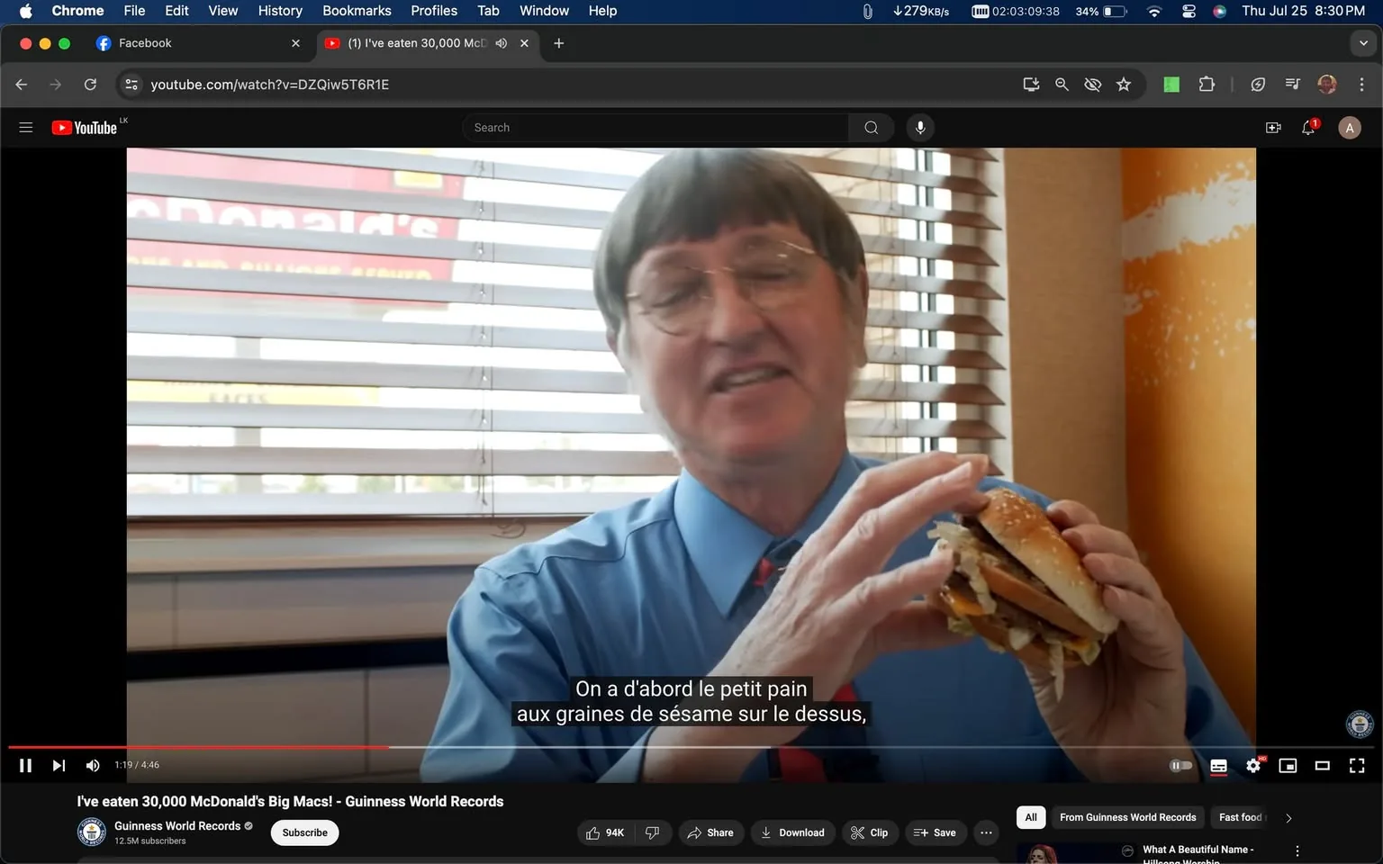 1) Rich description (8–12 sentences): The screenshot captures a moment from a YouTube video titled "I've eaten 30,000 McDonald's Big Macs! - Guinness World Records" on the Guinness World Records channel. The scene is set inside what appears to be a McDonald's restaurant, indicated by the branding visible through the window blinds in the background. A man, wearing a blue shirt and red tie, is holding a Big Mac in his hands. The man seems to be enthusiastically discussing the burger, indicated by his expressive hand movements and the subtitles present. The lighting is bright, typical of a fast-food restaurant during the day, and the blinds suggest an attempt to control sunlight in the space. The man's attire and the setting give a casual yet informative atmosphere, fitting for a record-themed discussion. The image captures a close-up view, focusing on the man's upper body and the burger, which serves as a central subject in the narrative. This visual context is enhanced by French subtitles at the bottom, translating his explanation of the burger's components. The video likely features a personal story or testimonial, exploring the man's unique Guinness World Record achievement related to consuming a large number of Big Macs.
2) On-screen text block:
- Title: "I've eaten 30,000 McDonald's Big Macs! - Guinness World Records"
- Channel / profile: "Guinness World Records"
- Site / app: "YouTube"
- Captions / subtitles: "On a d'abord le petit pain aux graines de sésame sur le dessus,"