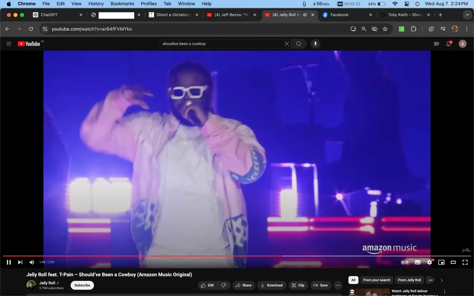 The image is a frame from a YouTube video titled "Jelly Roll feat. T-Pain – Should’ve Been a Cowboy (Amazon Music Original)." The scene depicts a live performance featuring T-Pain. He is wearing a white outfit with a light-colored jacket and distinctive white sunglasses. T-Pain is holding a microphone and performing on stage, emphasizing his charismatic presence. The background is lit with vibrant purples and blues, creating a dynamic concert atmosphere. The lighting adds to the energetic vibe of the performance. The Amazon Music logo is visible in the lower right corner, indicating the video’s affiliation with Amazon Music. The video is hosted on Jelly Roll’s YouTube channel, which has 3.79 million subscribers. The performance seems lively and engaging, capturing the essence of a live musical event.
- Title: "Jelly Roll feat. T-Pain – Should’ve Been a Cowboy (Amazon Music Original)"
- Channel / profile: "Jelly Roll"
- Site / app: "YouTube"