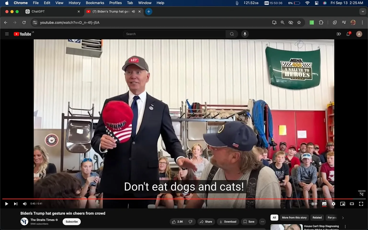 In this YouTube screenshot, the scene captures an indoor event where a man, identified by the hint as Biden, is holding a red hat with "TRUMP 2024" printed on it. He is dressed in a formal black suit and tie, conveying a sense of professionalism, with a gray cap marked "627" on his head. The backdrop features a group of seated audience members, including men, women, and children, indicative of a community gathering or public speech setting. The room appears to be a workshop or garage, with tools and hardware visible in the background. A green banner with "MBNA 400 A SALUTE TO HEROES" is prominently displayed on the wall, adding a touch of local event branding to the scene. The subtitle "Don't eat dogs and cats!" is humorously juxtaposed, suggesting a light-hearted moment or a specific point being emphasized during the speech. The atmosphere appears casual and engaging, with audience members attentively listening, some smiling, while others appear curious. The screenshot is part of a video titled "Biden’s Trump hat gesture win cheers from crowd," featured on The Straits Times channel, highlighting a moment of interaction that elicited a positive reaction from the crowd.