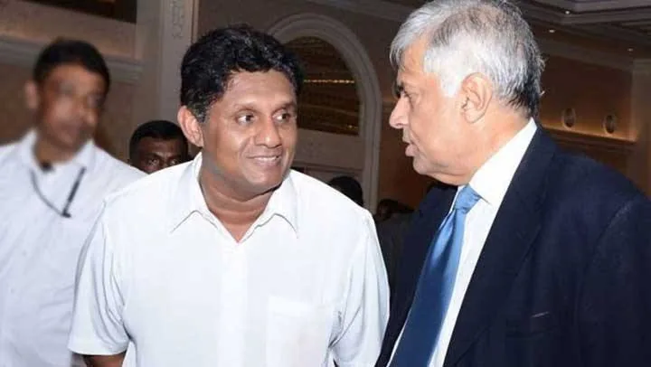 1) Rich description: The image captures an indoor scene featuring two prominent figures, Ranil Wickremasinghe and Sajith Premadasa, engaged in conversation. Ranil Wickremasinghe is dressed in a dark suit with a light blue tie, exuding a formal and professional appearance. He is turned slightly towards Sajith Premadasa, who is wearing a casual white shirt, giving a more relaxed vibe. The setting appears to be a formal event or gathering, likely in a hotel or conference hall, indicated by the elegant decor in the background. There are a few other people visible in the background, but they are out of focus, suggesting that the interaction between Wickremasinghe and Premadasa is the focal point of the scene. The lighting is warm and soft, typical of indoor event settings, creating a congenial atmosphere. Both individuals seem engaged in a cordial exchange, as suggested by their body language and expressions.
2) On-screen text block:
- Title: ""