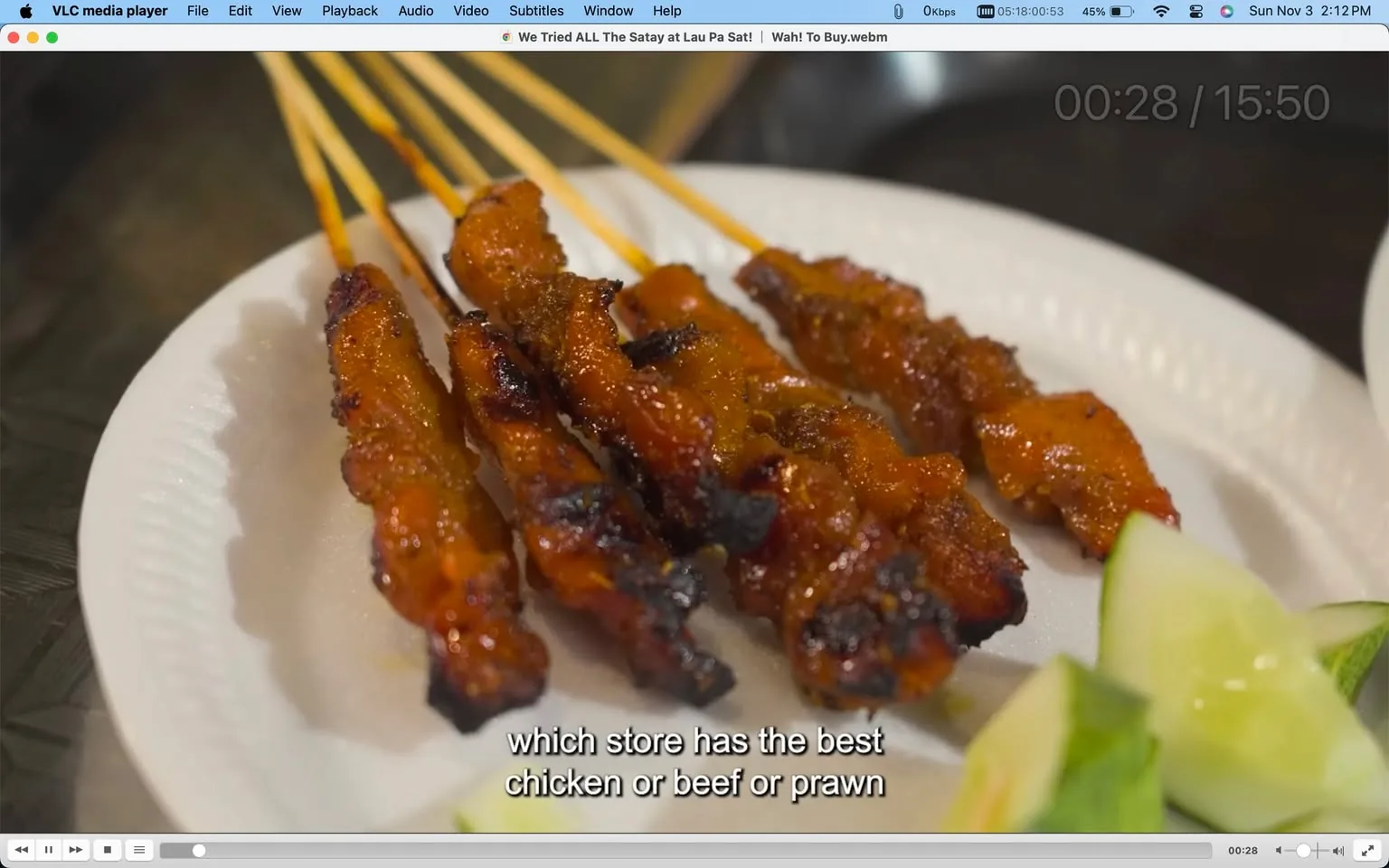 1) Rich description: The image is a video frame showing a close-up of Chicken Satay, skewered meat pieces, displayed on a white disposable plate. The satay is richly glazed, with a slightly charred appearance, suggesting it has been grilled. The plate is accompanied by slices of fresh cucumber on the side, adding a touch of green to the composition. The lighting is warm, enhancing the glossy texture of the satay. The video frame is from a video titled "We Tried ALL The Satay at Lau Pa Sat! Wah! To Buy," viewed using VLC media player. The scene captures the appetizing look of the satay, focusing on its rich color and succulent appearance. Overlaid subtitles question which store has the best type of satay, indicating a taste comparison or review theme in the video. The environment seems to be an indoor setting, possibly a food market or restaurant, dedicated to exploring various satay offerings.
2) On-screen text block:
- Title: "We Tried ALL The Satay at Lau Pa Sat! Wah! To Buy"
- Site / app: "VLC media player"
- Captions / subtitles: "which store has the best chicken or beef or prawn"
