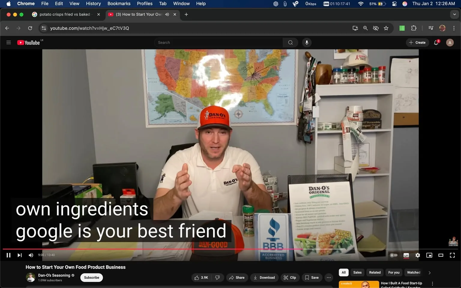 In the image, an unidentified adult male is seated at a desk, gesturing with his hands as he speaks. He is wearing a white shirt with the logo "Dan-O's" and an orange cap with the same branding. The background features a colorful map of the United States, and there are various items on the desk, including a canister of seasoning, a brochure for Dan-O's, and a sign indicating BBB accreditation. The setting appears to be an indoor office or workspace, with shelves displaying additional products and materials related to the food business. The text overlay suggests he is discussing the importance of using one's own ingredients and the value of online resources.
