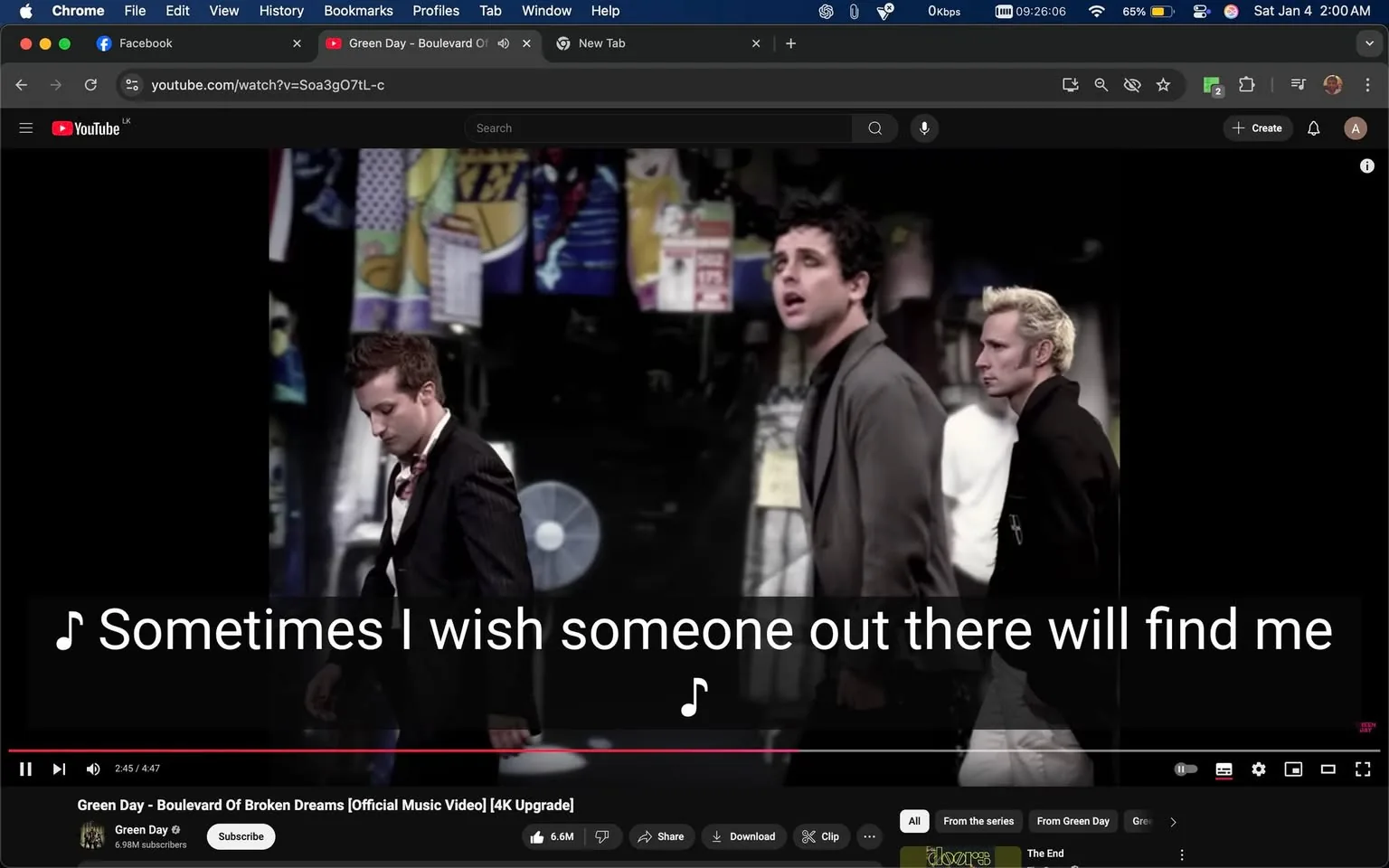 In the scene from a music video, three unidentified male figures are walking in a city-like setting, with a backdrop of colorful posters and banners. The first figure, dressed in a black suit, appears to be looking down, while the second figure, in a gray coat, is singing with a contemplative expression. The third figure, wearing a white shirt and black jacket, walks with a serious demeanor. The lyrics "Sometimes I wish someone out there will find me" are prominently displayed on the screen, indicating a theme of longing or searching. The setting suggests an urban environment, possibly at night, given the lighting and the presence of various advertisements. The video is hosted on YouTube, as indicated by the interface elements visible at the bottom of the screen.