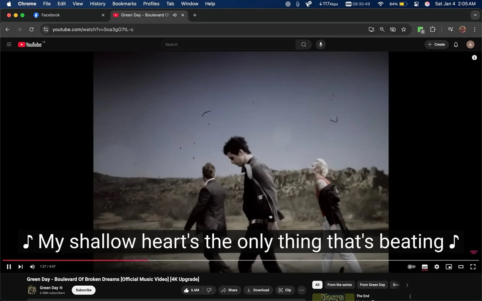 In the scene from a music video, three individuals are walking along a barren landscape, with a clear sky above. The person in the center appears to be wearing a black jacket and has dark hair, while the others are dressed in suits. The lyrics "My shallow heart's the only thing that's beating" are prominently displayed on the screen, suggesting an emotional theme. The background features rocky terrain, enhancing the desolate atmosphere. The video is part of a song by Green Day, as indicated by the title in the video description. The overall mood seems reflective, aligning with the lyrical content.
